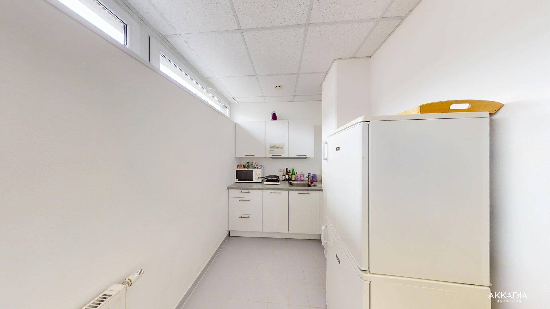 Kleine Küchenzeile mit weißen Schränken, Mikrowelle und Kühlschrank in einem funktionalen Raum.