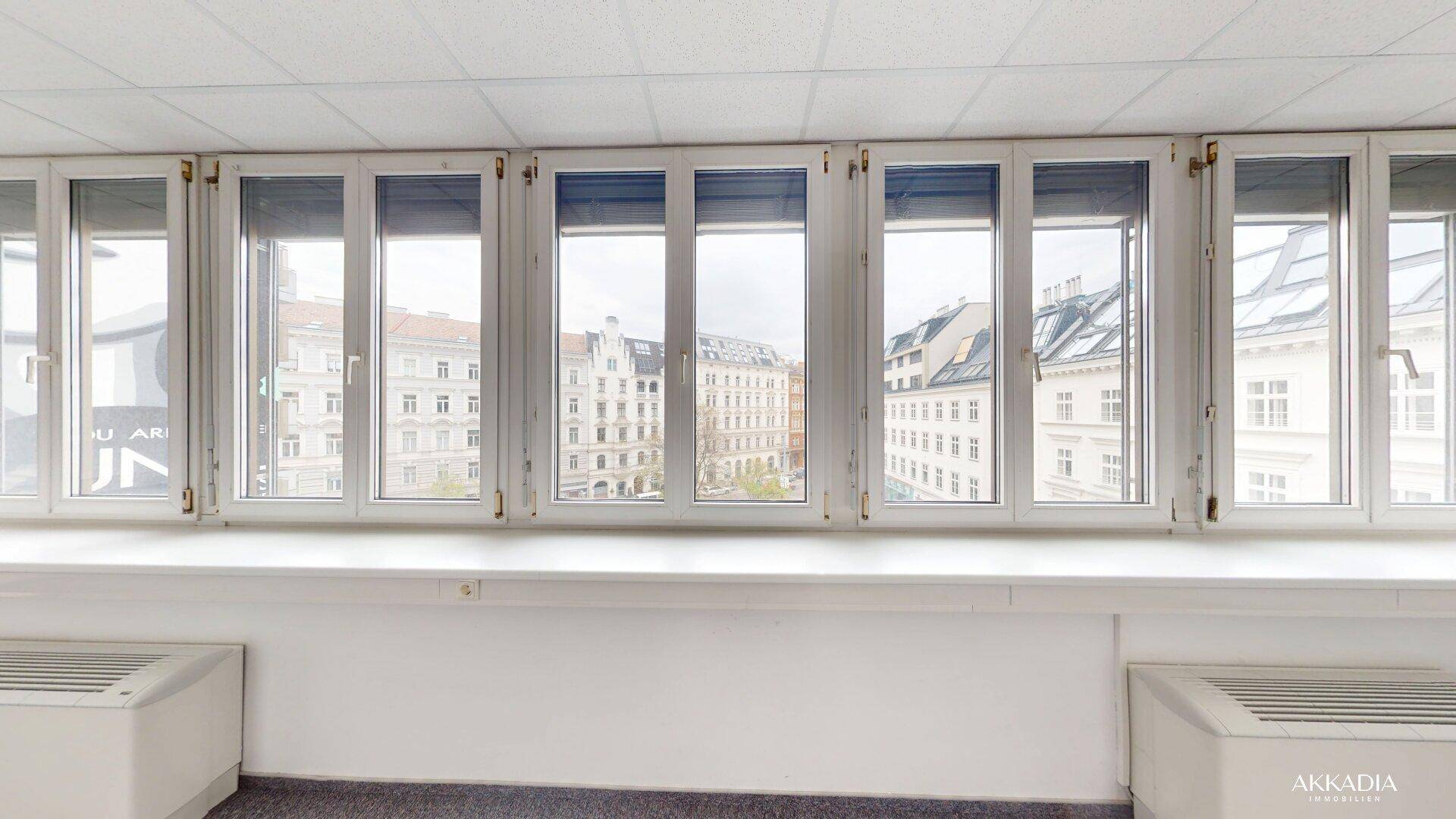 Reihe von Fenstern mit Blick auf die umliegenden Gebäude und die Stadt, mit Heizkörpern darunter.