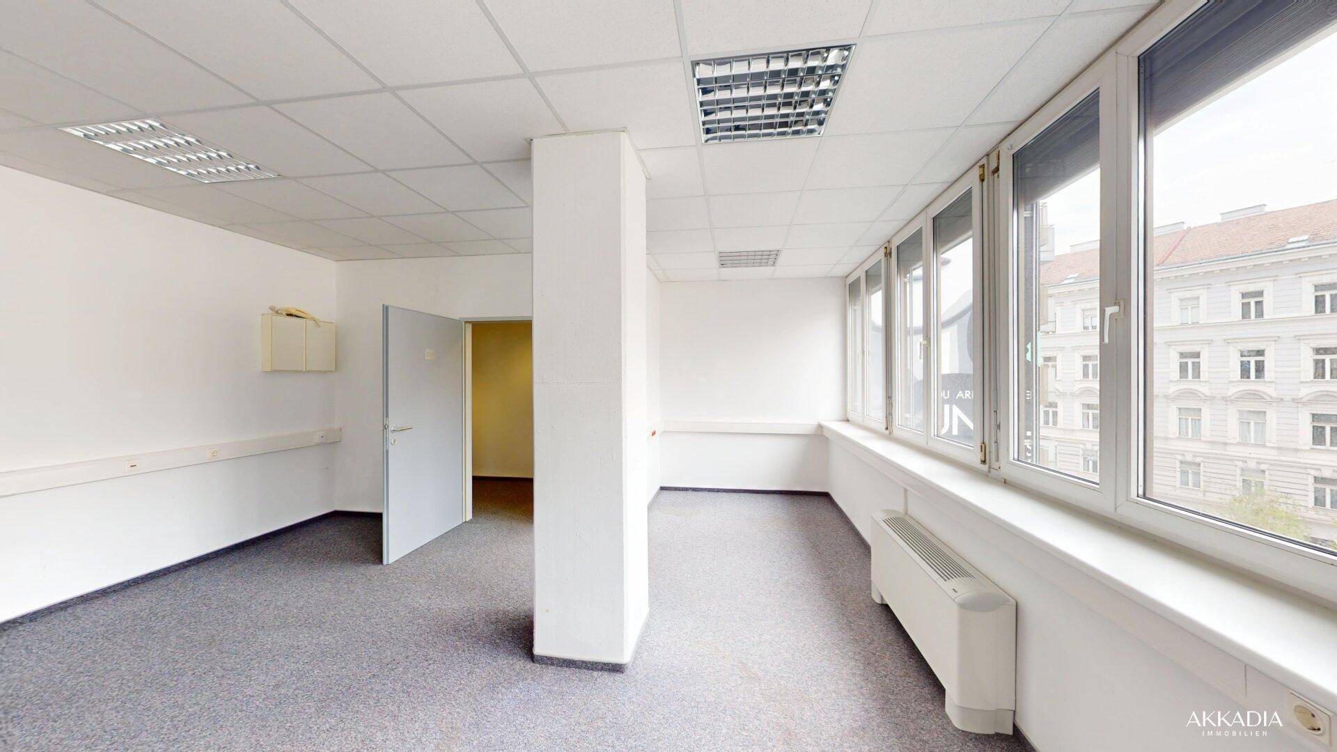 Helles Büro mit Teppichboden, Säule und Fensterfront, die einen weiten Blick auf die Stadt bietet.