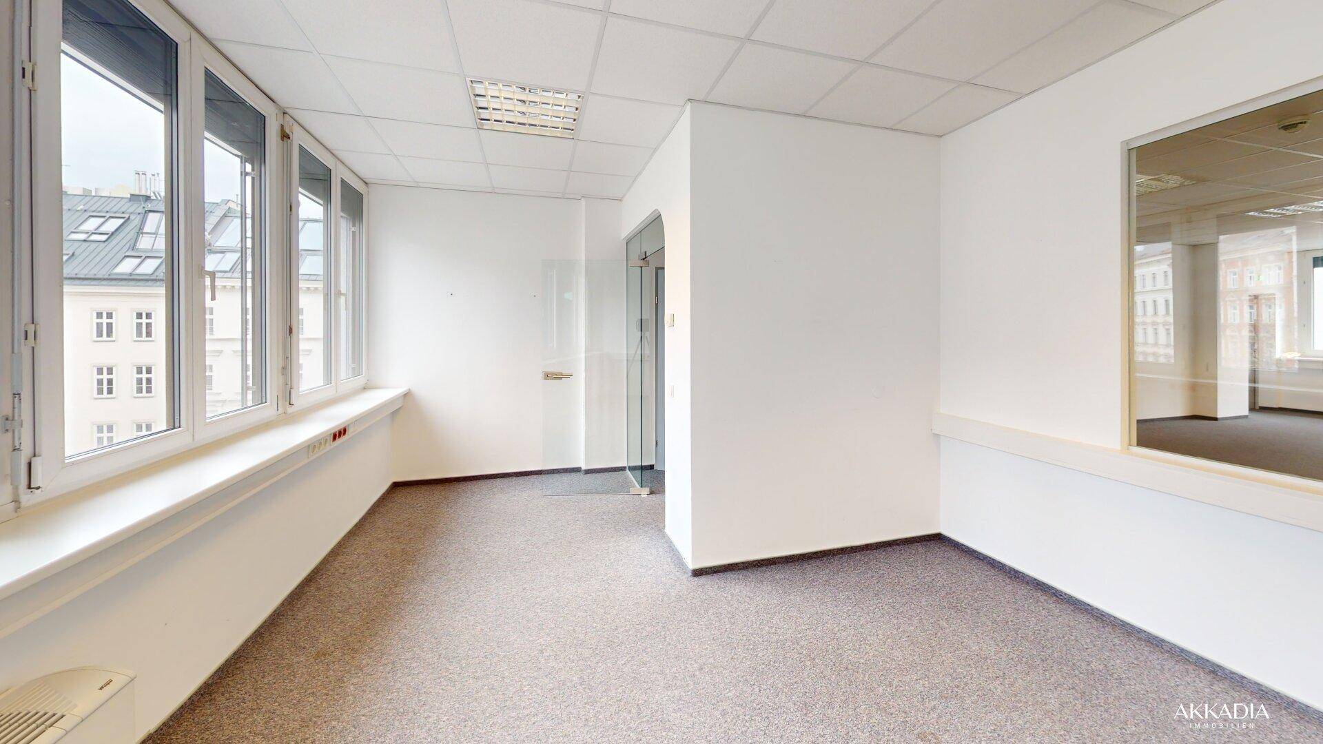 Helles Büro mit Teppichboden, großen Fenstern und Blick auf die Stadt, ausgestattet mit Rasterdecken.