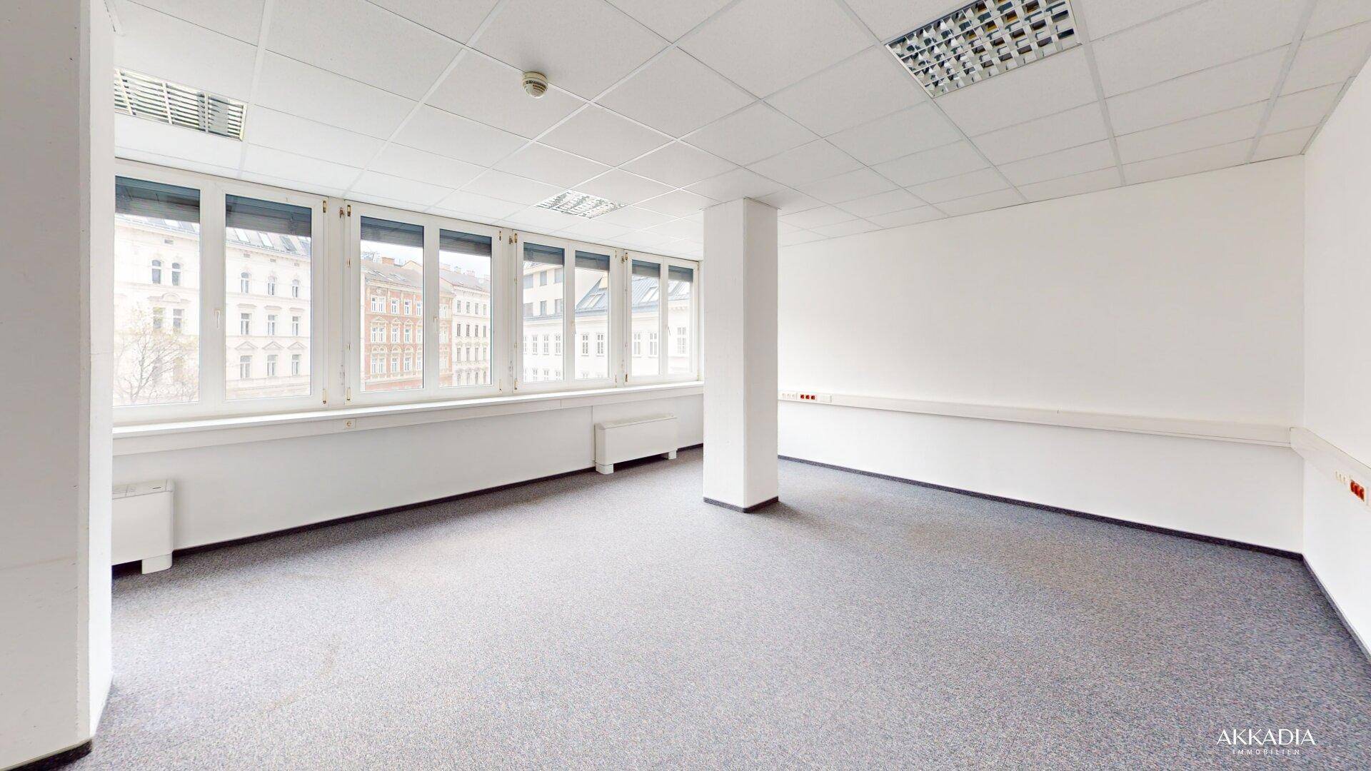 Geräumiges Büro mit Teppichboden, Säule und Fensterfront, die den Raum mit Tageslicht durchflutet.