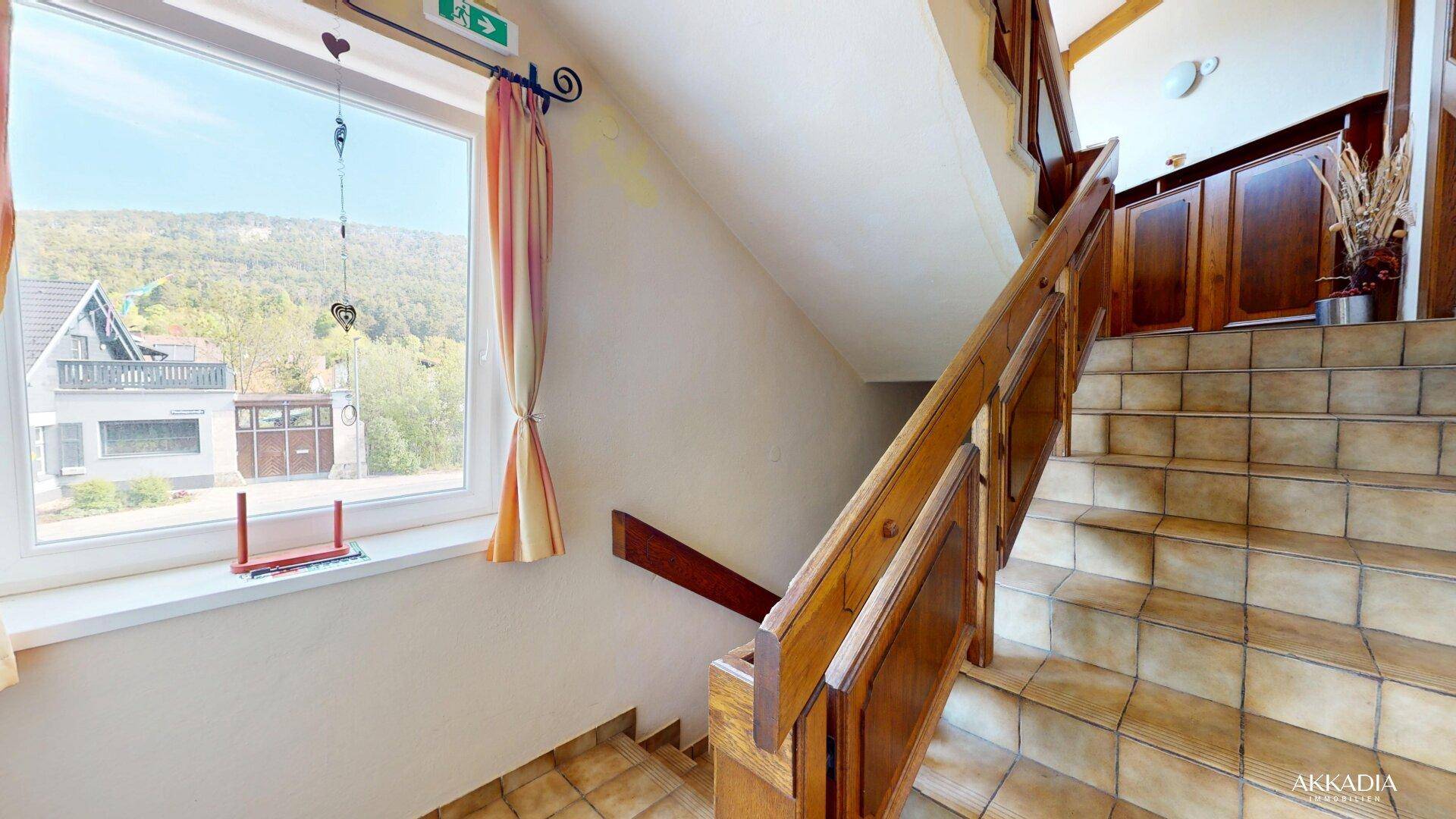 Helles Treppenhaus mit Holzgeländer und gefliesten Stufen, mit Blick auf die umliegende Landschaft.