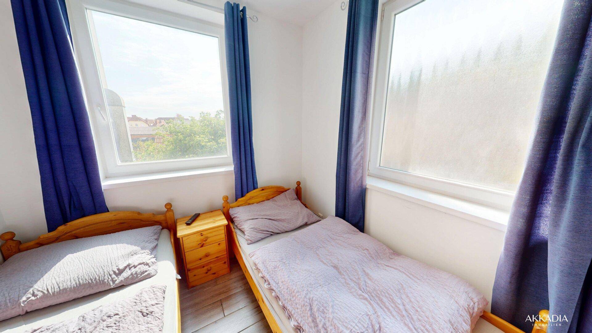 Helles Schlafzimmer mit zwei Einzelbetten, Holzfußboden und blauen Vorhängen.