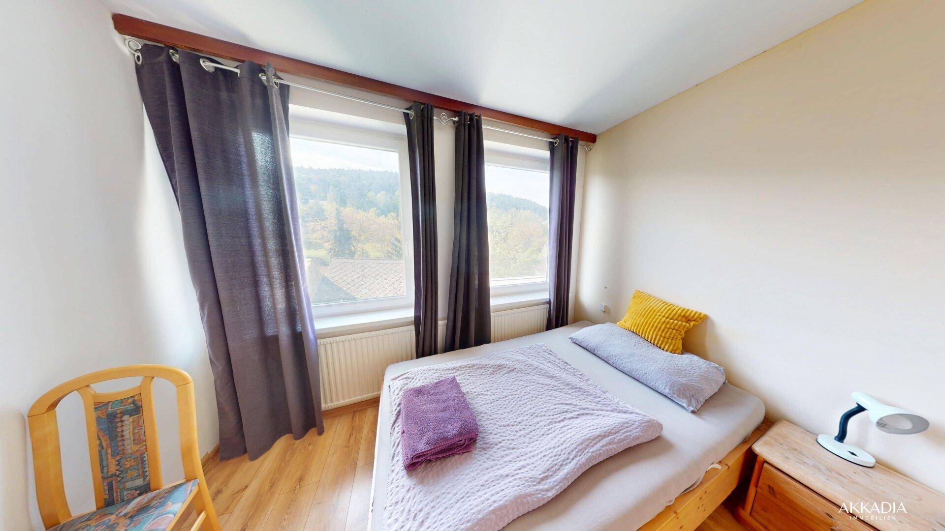 Helles Schlafzimmer mit Einzelbett, Holzfußboden und Fenstern mit Blick ins Grüne.