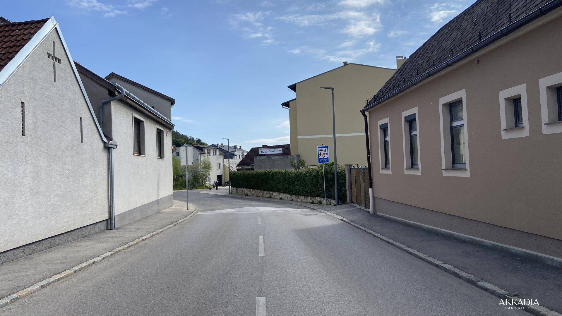 Ruhige Wohnstraße mit gepflegten Häusern und grüner Hecke unter blauem Himmel.