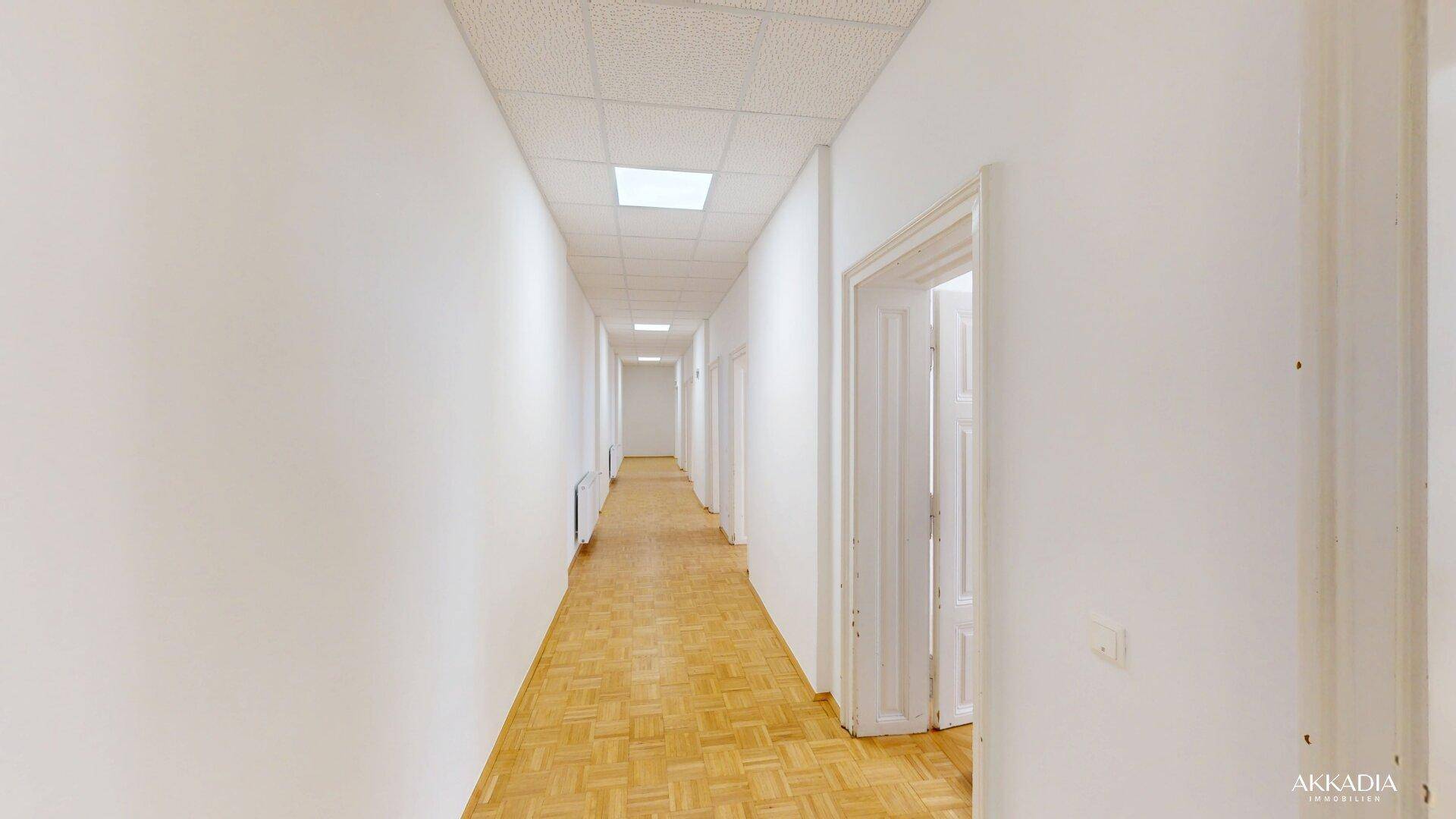 Langer, heller Flur mit Fischgrätparkett und mehreren Türen, gut beleuchtet.