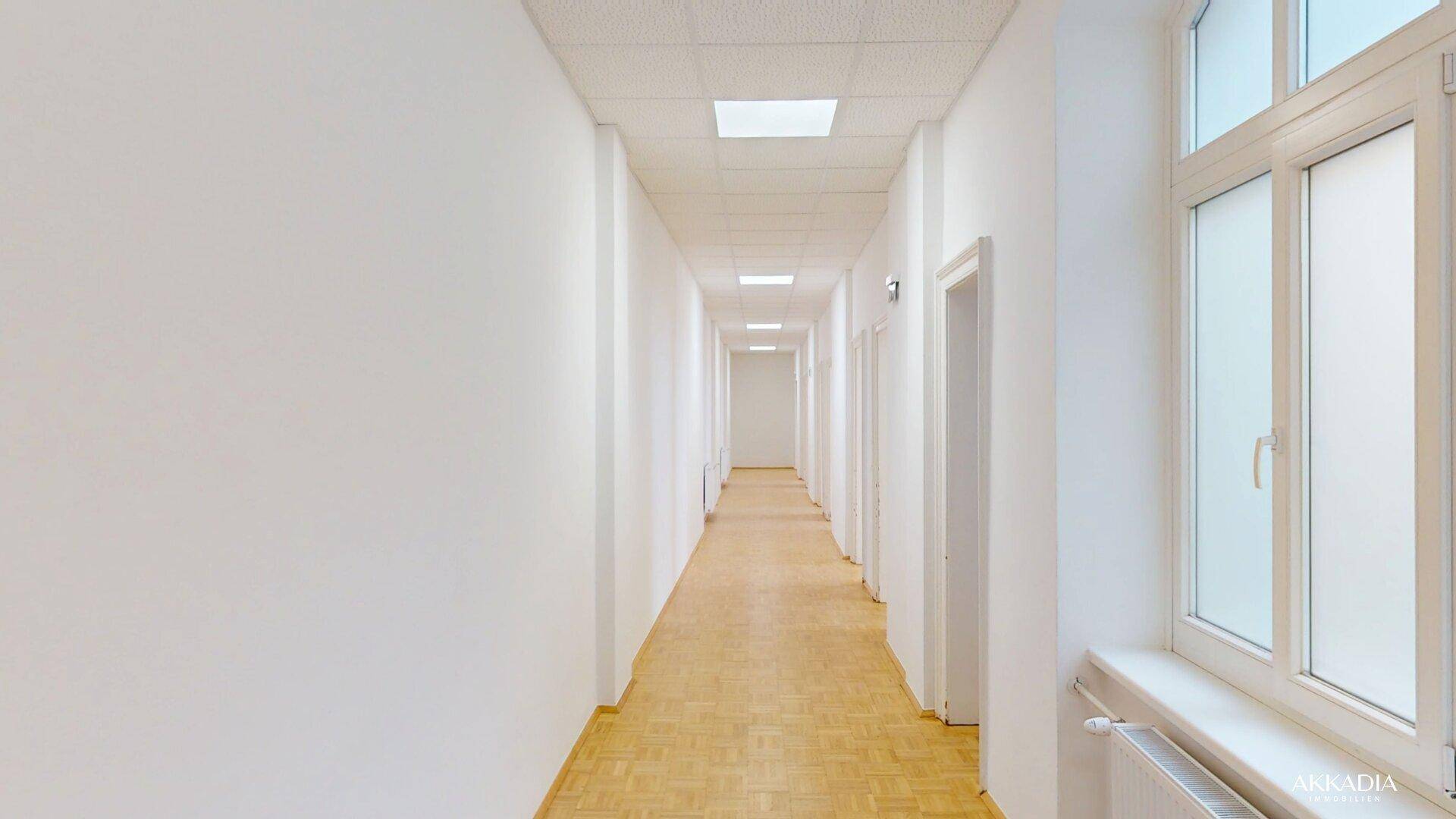 Langer, heller Flur mit Fischgrätparkett und mehreren Türen, gut beleuchtet.