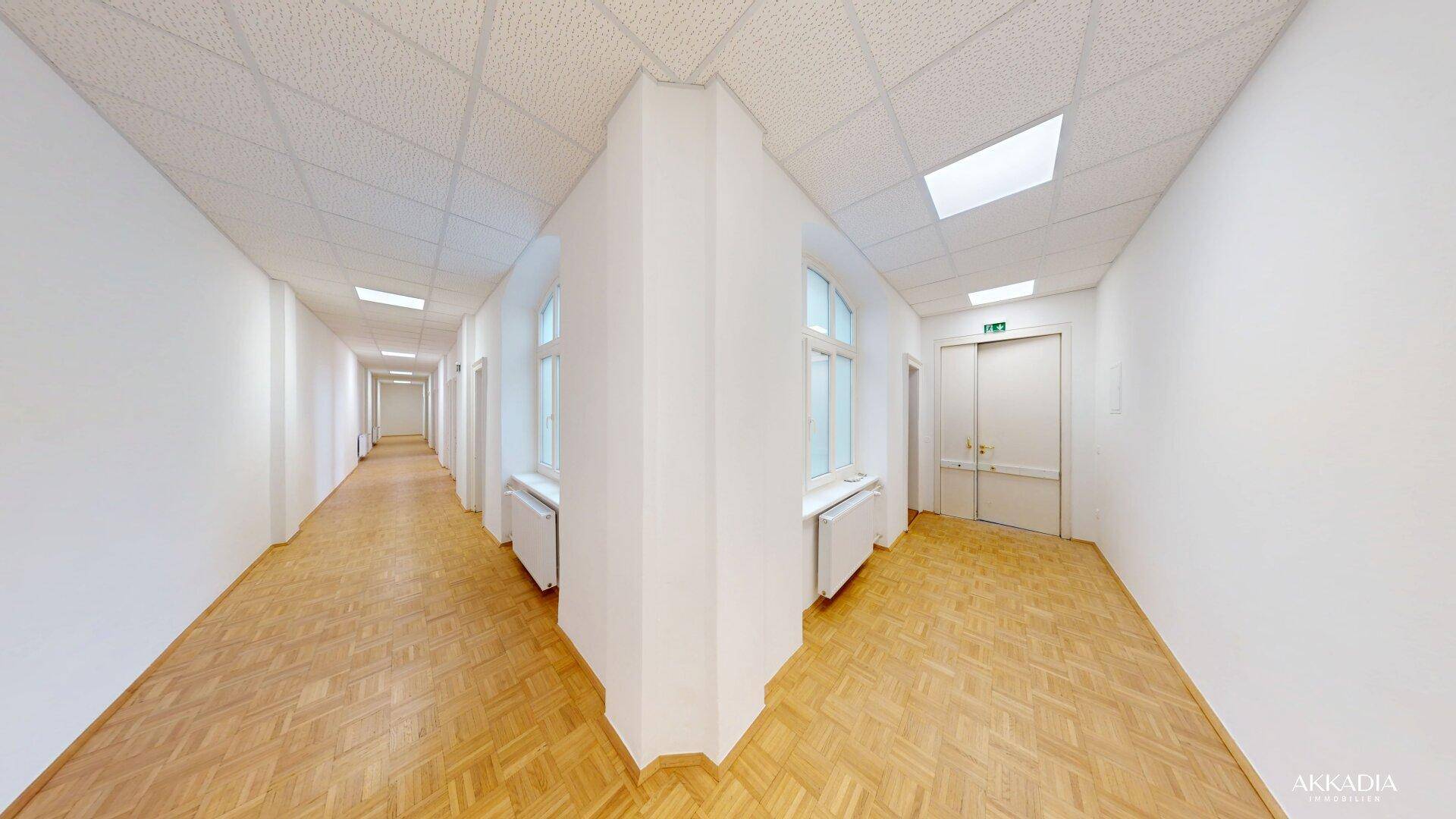 Langer, heller Flur mit mehreren Fenstern und Fischgrätparkett, gut beleuchtet.