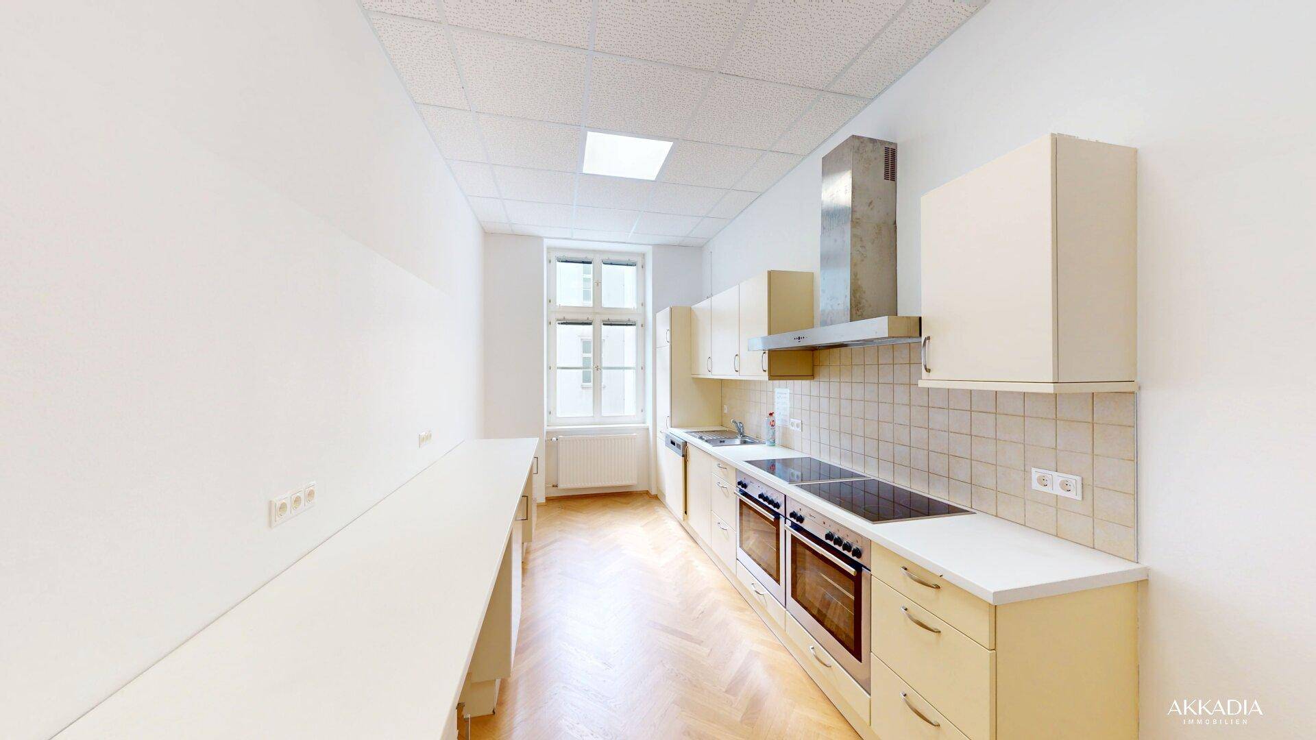 Funktionale Küche mit beigen Schränken, Herd und Dunstabzugshaube, gut beleuchtet.
