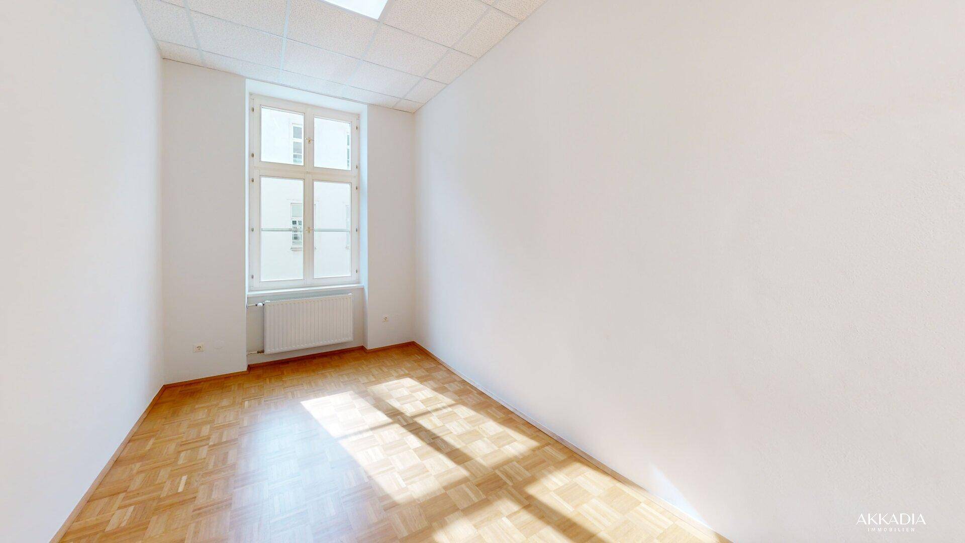 Heller Raum mit Fischgrätparkett und einem Fenster, durch das Sonnenlicht einfällt.