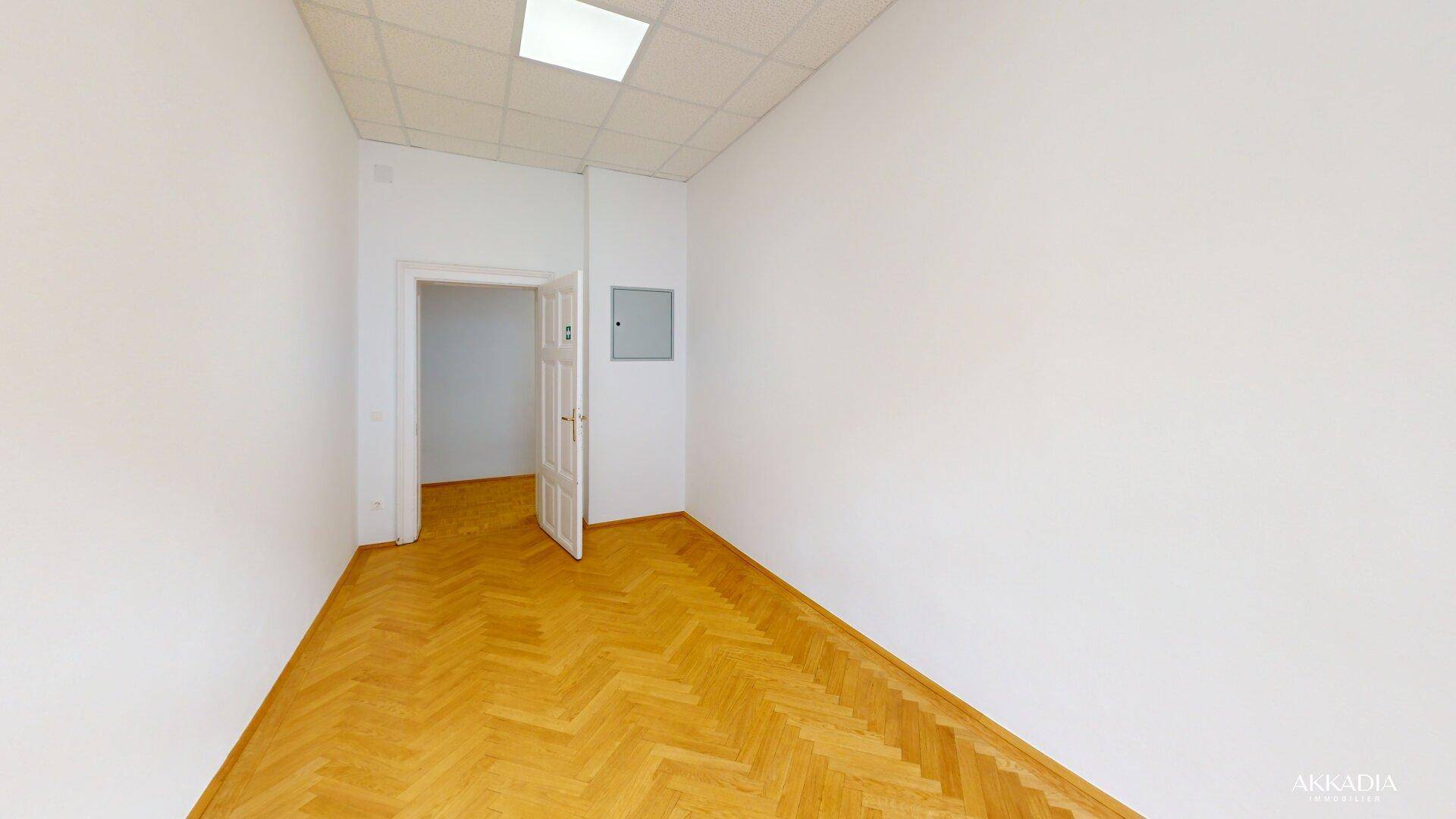 Leerer Raum mit Fischgrätparkett und weiß gestrichenen Wänden, mit offener Tür.