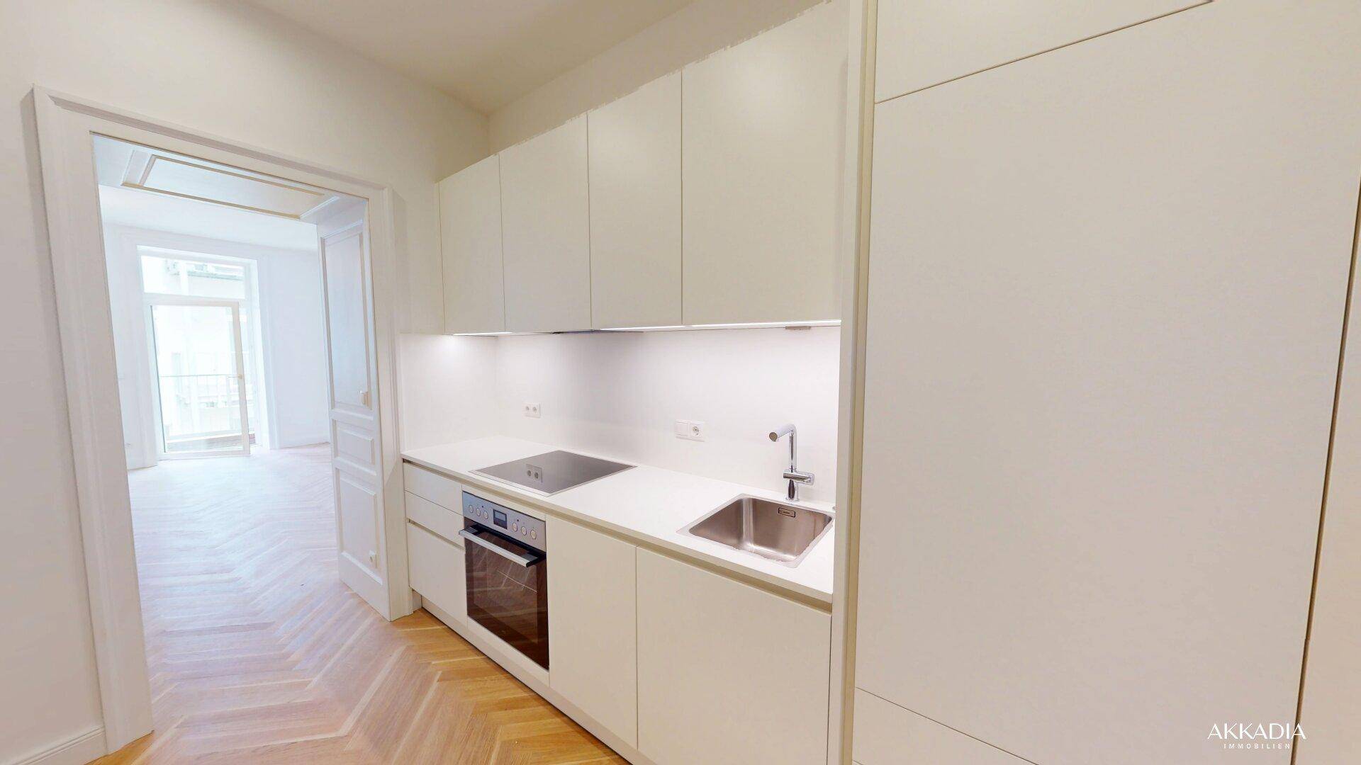 Moderne Einbauküche mit weißen Schränken, integrierten Geräten und Blick auf einen weiteren Raum.
