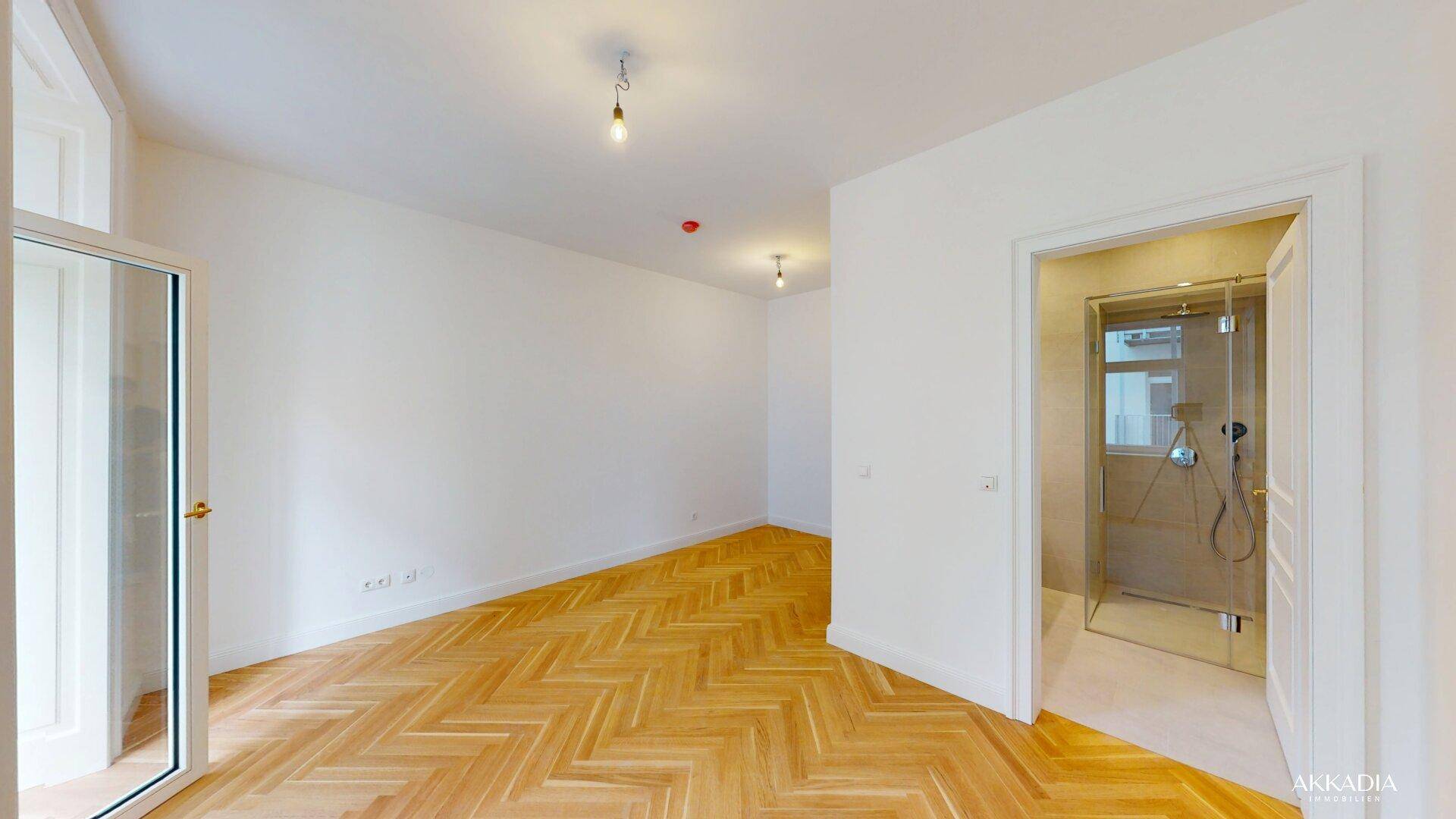 Geräumiges, helles Zimmer mit Fischgrätparkett und Zugang zu einem modernen Badezimmer.