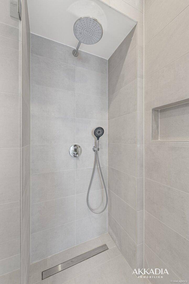 Geräumige, moderne Duschkabine mit Regendusche und Handbrause in hellen Fliesen.