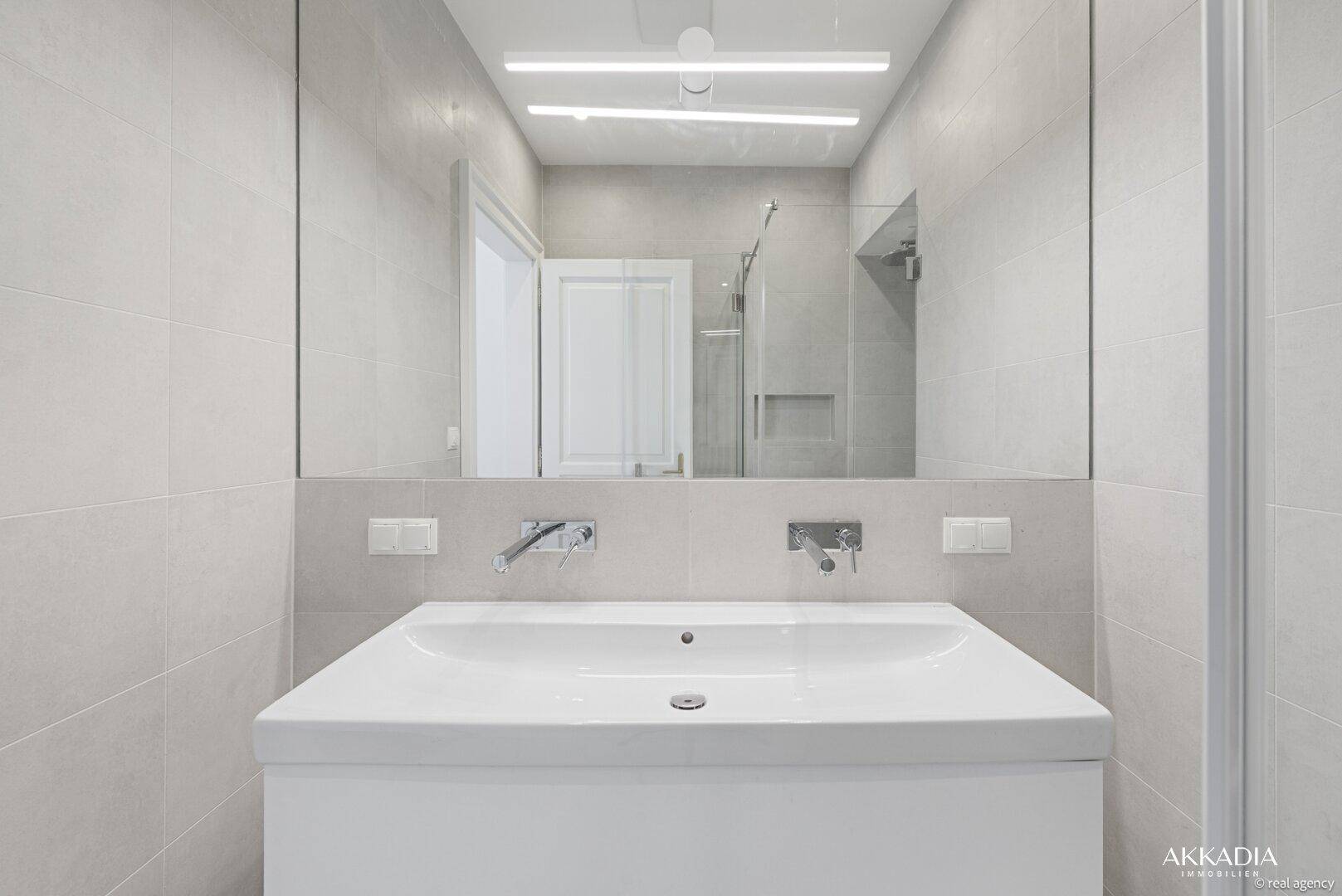 Modernes Badezimmer mit großem Spiegel, beleuchtetem Waschtisch und Einzelwaschbecken.