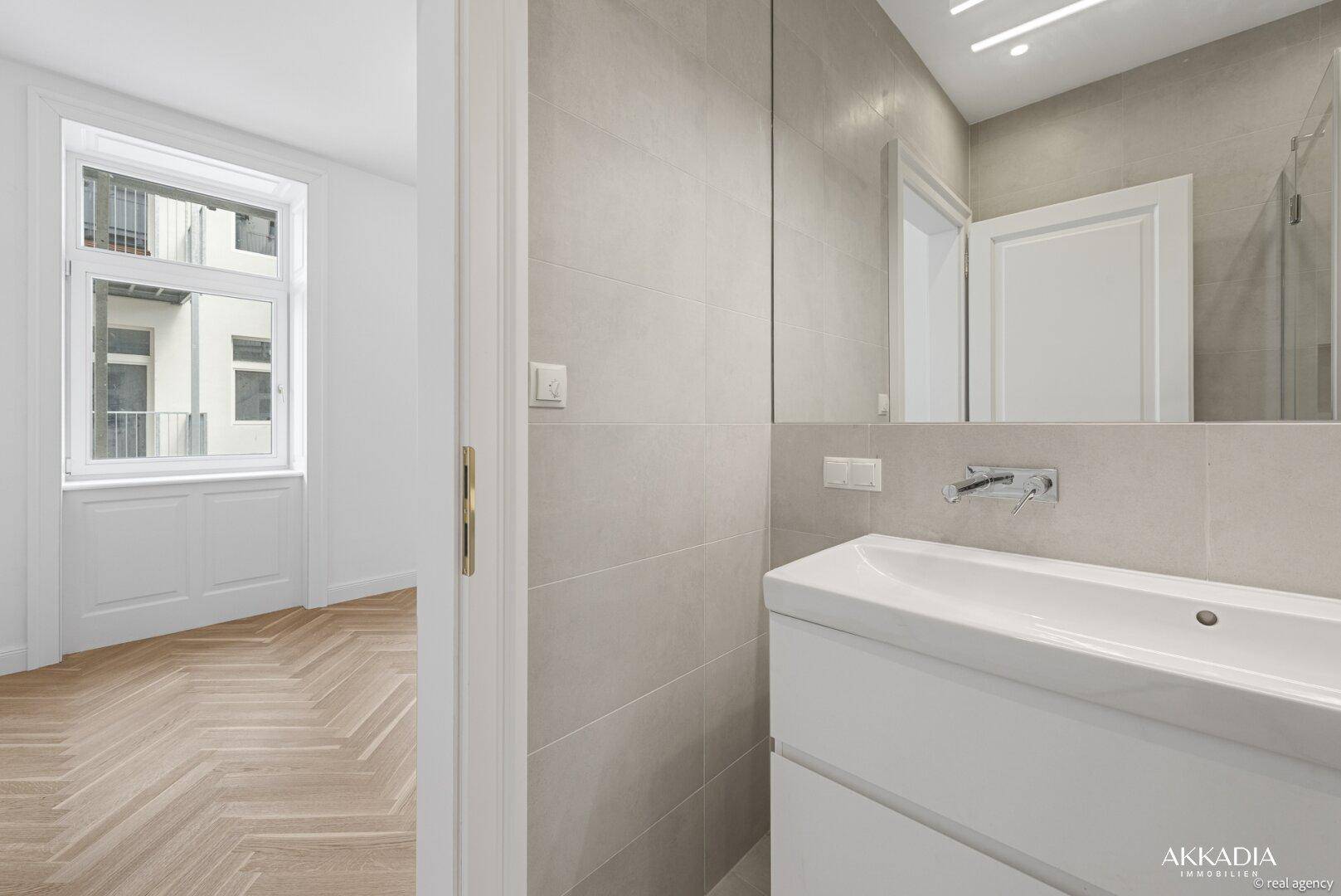 Modernes Badezimmer mit Waschtisch und Spiegel, mit Blick in ein helles Zimmer.