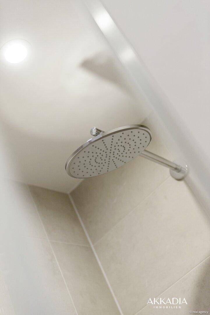 Regendusche in einem modernen Badezimmer mit hellen Fliesen und minimalistischem Design.