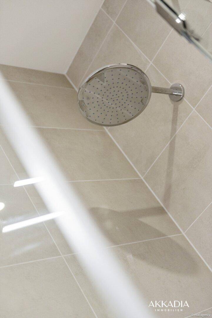Regendusche in einem modernen Badezimmer mit hellen Fliesen und minimalistischem Design.