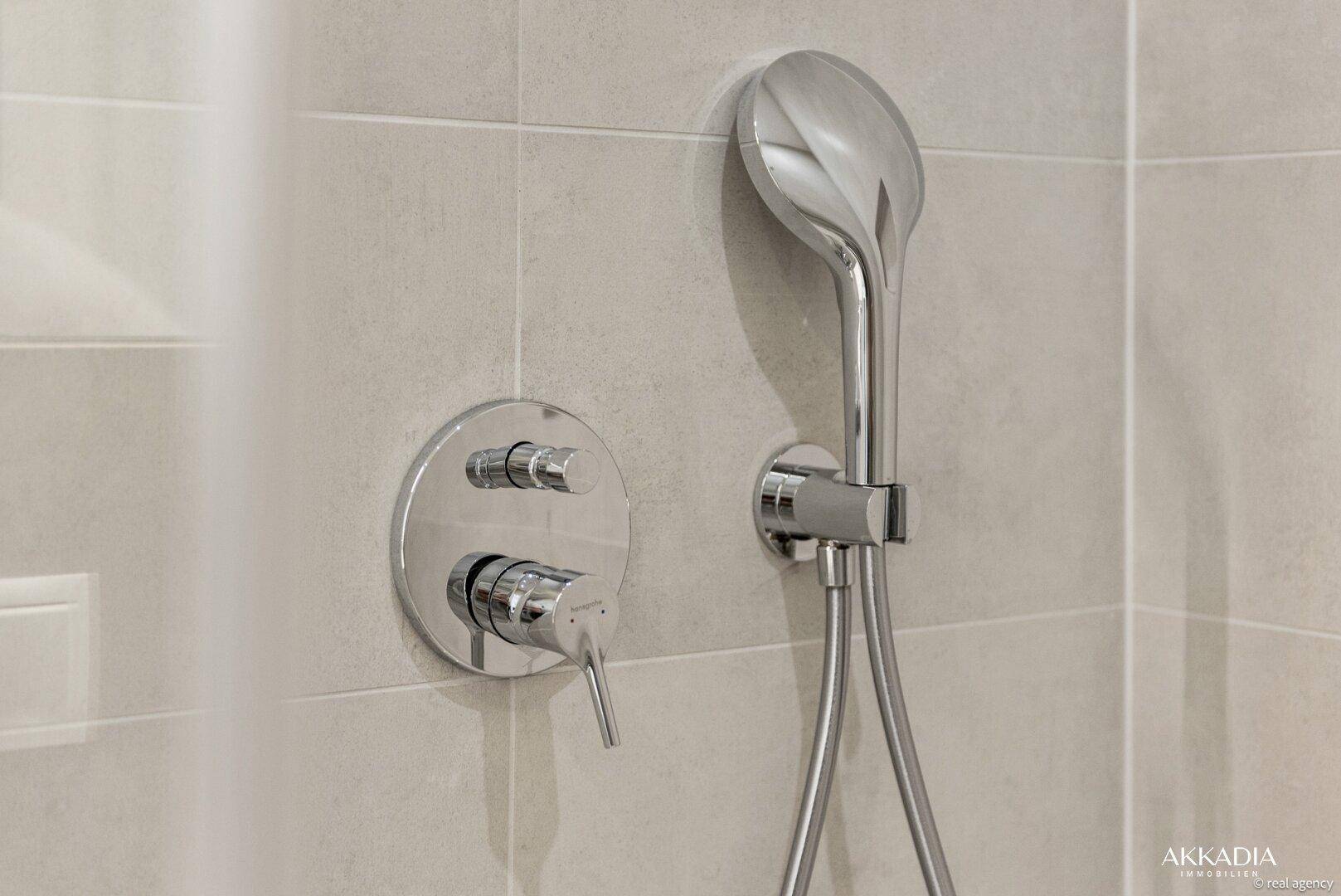 Moderne Duscharmatur mit Handbrause und hellen Fliesen in einem gepflegten Badezimmer.