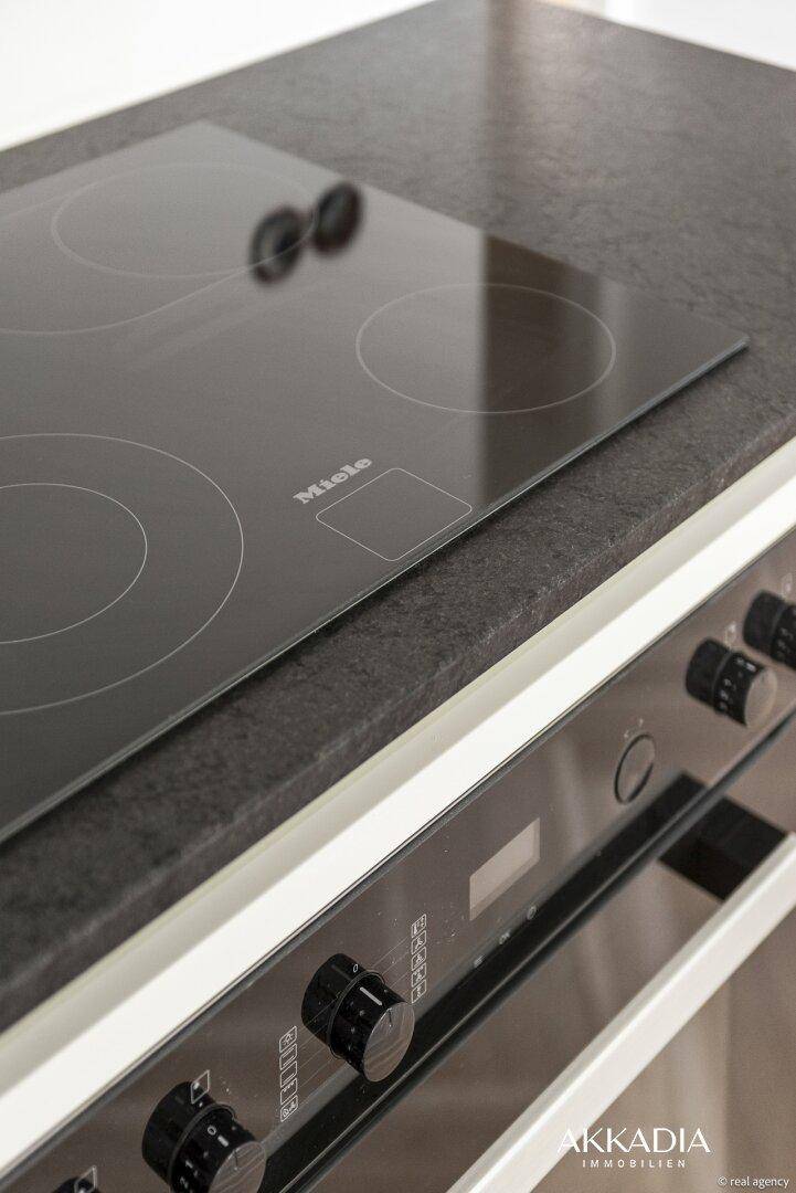 Miele Induktionskochfeld und Backofen in einer modernen Küche mit dunkler Granitarbeitsplatte.