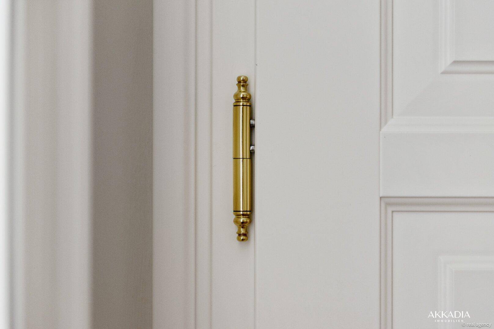 Detailansicht eines goldenen Türscharniers an einer klassischen weißen Innentür.