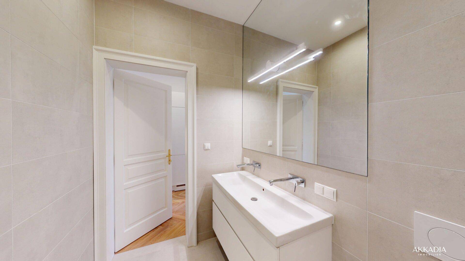 Modernes Badezimmer mit beigen Fliesen, Einzelwaschbecken und großem Spiegel.