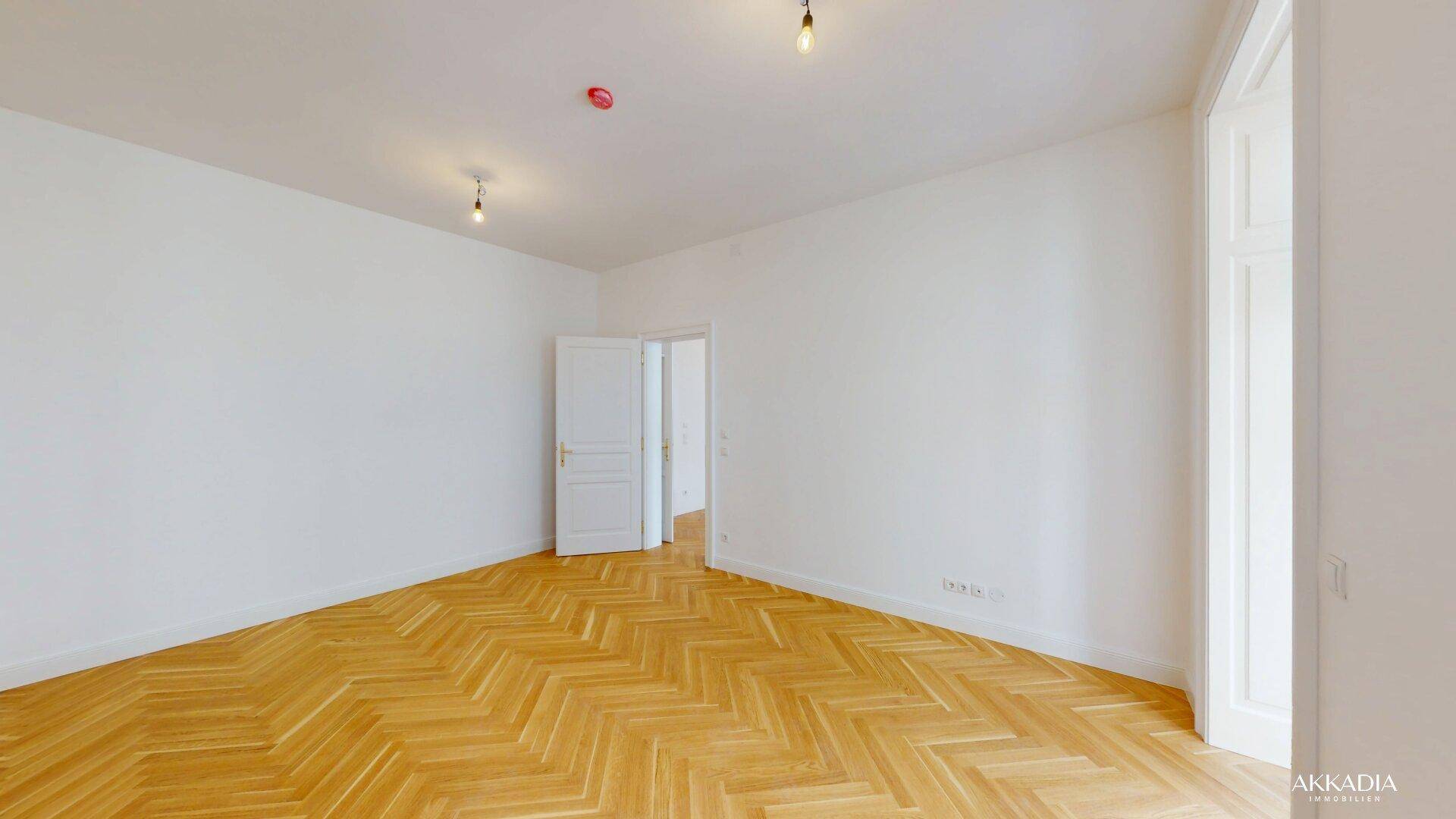 Leeres Zimmer mit Fischgrätparkett und weißen Wänden, ideal für Wohn- oder Schlafbereich.