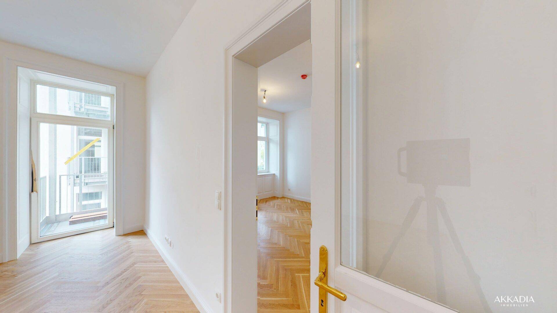 Heller Flur mit Fischgrätparkett und Zugang zu einem weiteren Zimmer sowie einem Balkon.