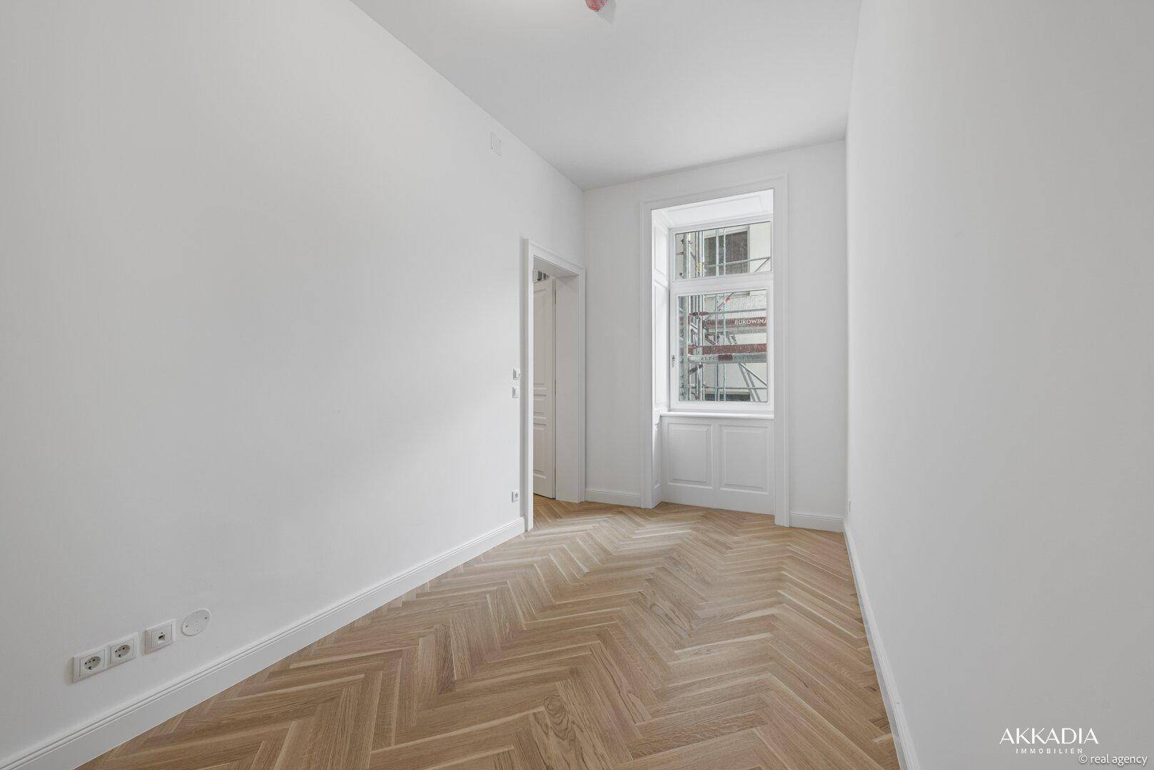 Kleines, helles Zimmer mit Fischgrätparkett und einem Fenster, ideal als Schlaf- oder Arbeitszimmer.
