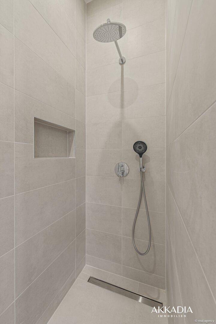 Geräumige, ebenerdige Dusche mit Regenduschkopf und beigen Wandfliesen.