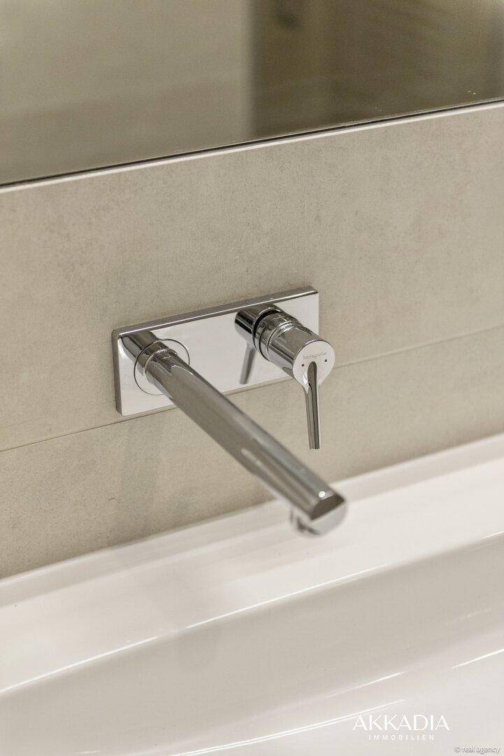 Moderner Wandhahn über einem weißen Waschbecken mit beigefarbenen Fliesen im Badezimmer.