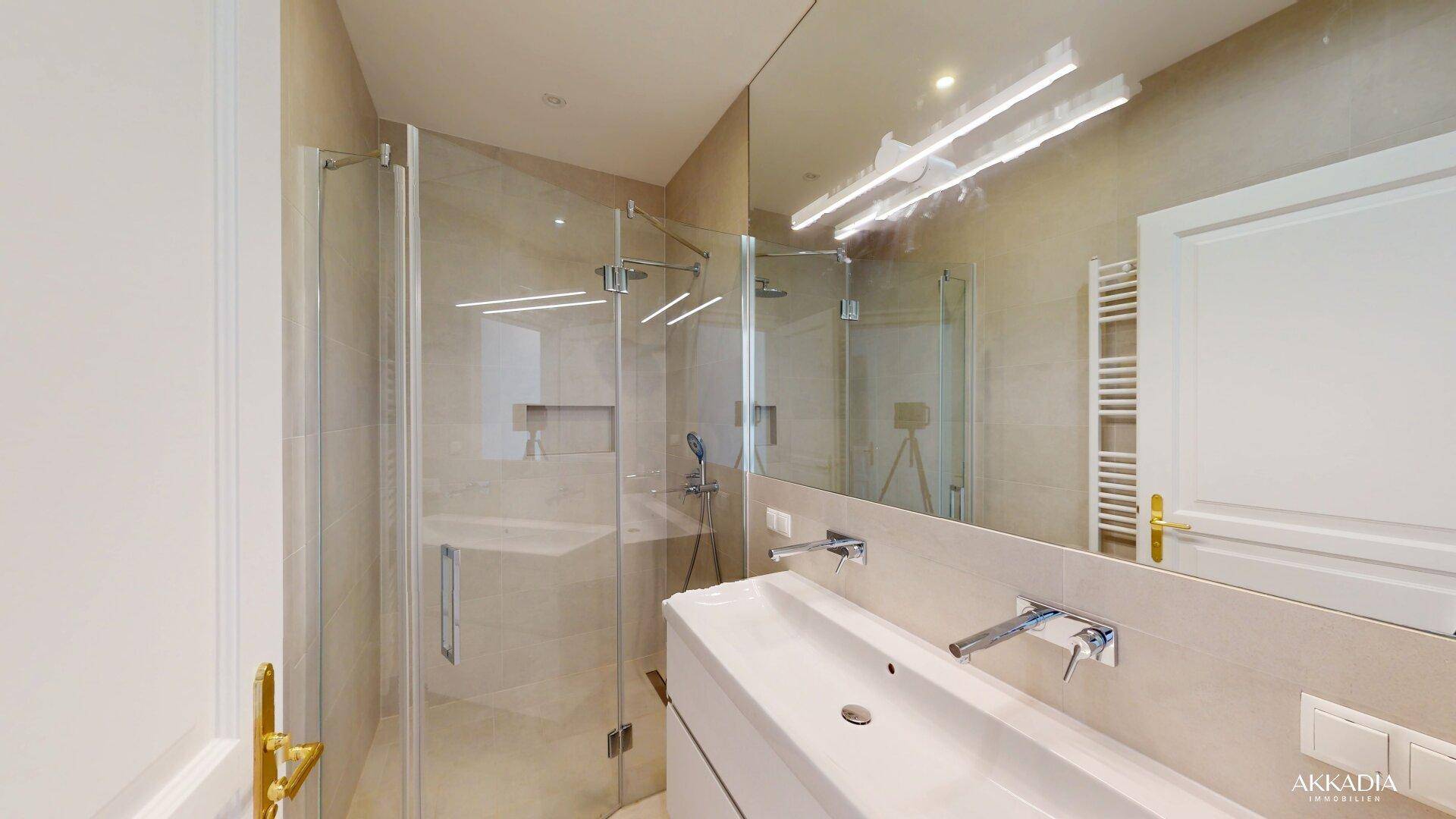 Modernes Badezimmer mit begehbarer Dusche, eleganten beigefarbenen Fliesen und großem Spiegel.