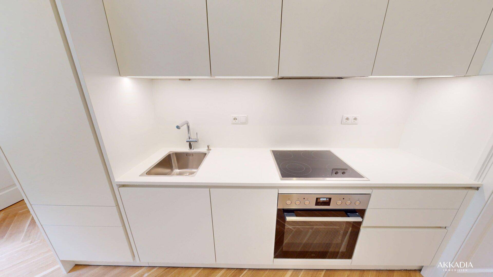 Moderne Küchenzeile mit weißen Schränken, Induktionskochfeld und integriertem Backofen.