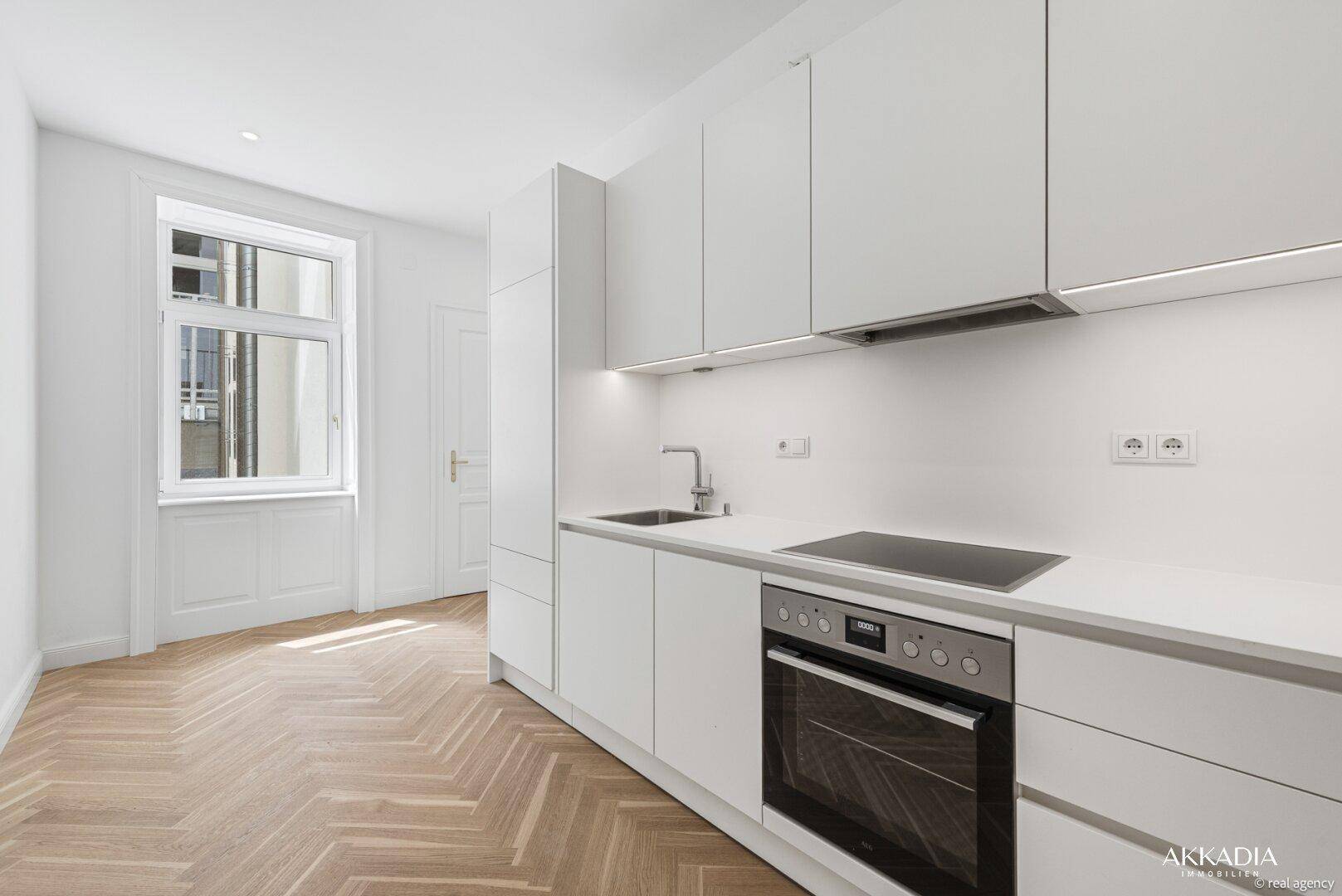 Moderne Küchenzeile mit weißen Schränken, Induktionskochfeld und Backofen, mit Fenster für Tageslicht.