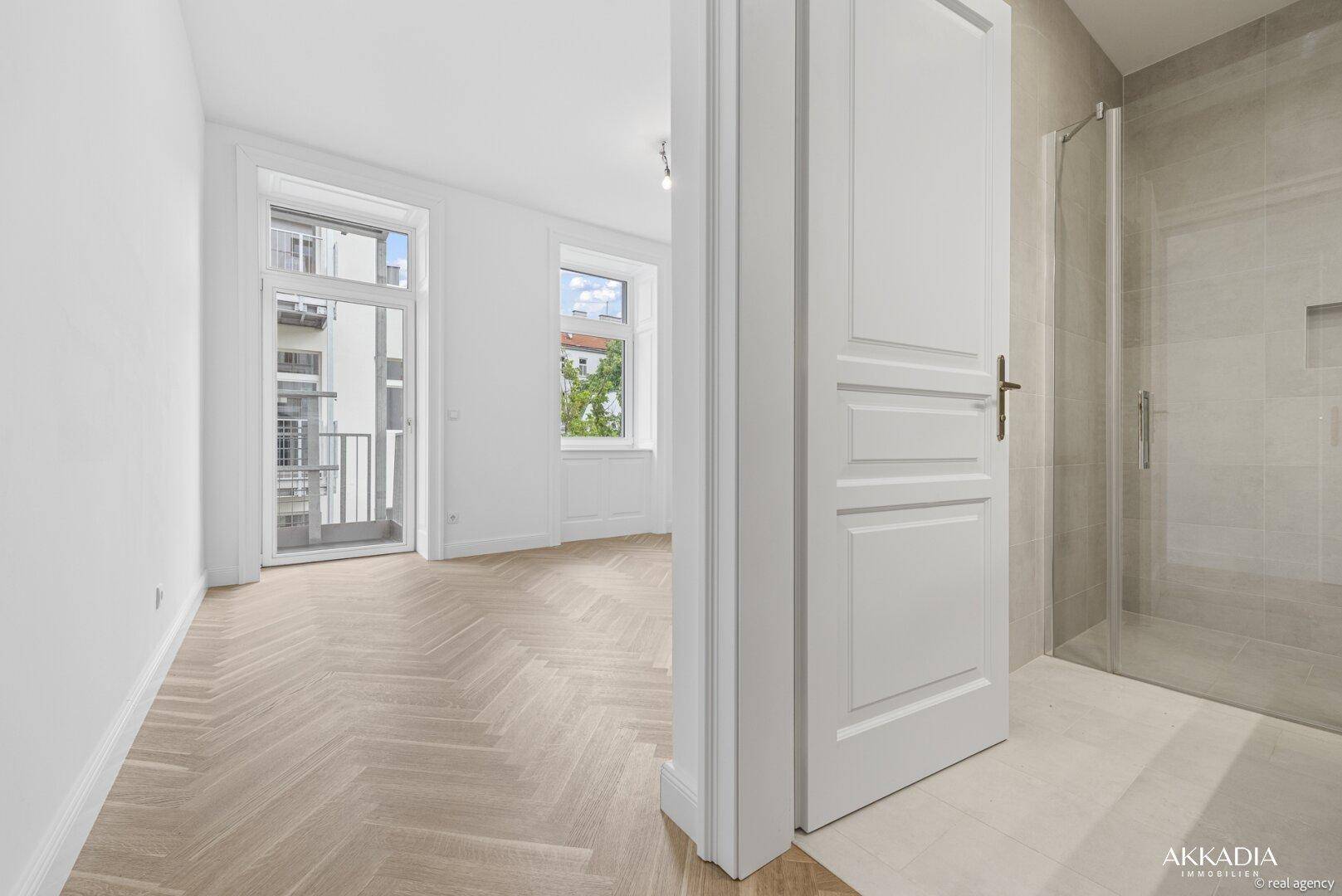 Geräumiges Wohnzimmer mit Fischgrätparkett, großen Fenstern und direktem Zugang zum Balkon.