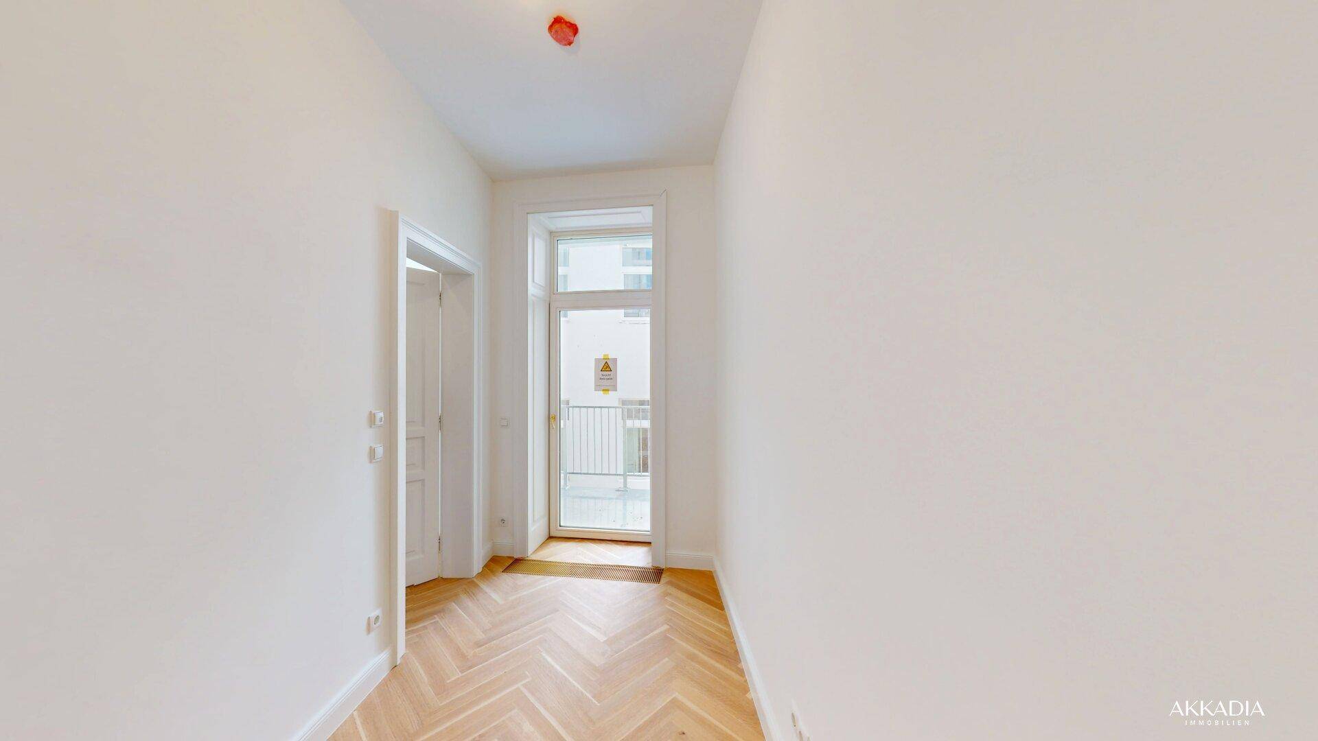 Heller Flur mit Fischgrätparkett und Zugang zu einem französischen Balkon.