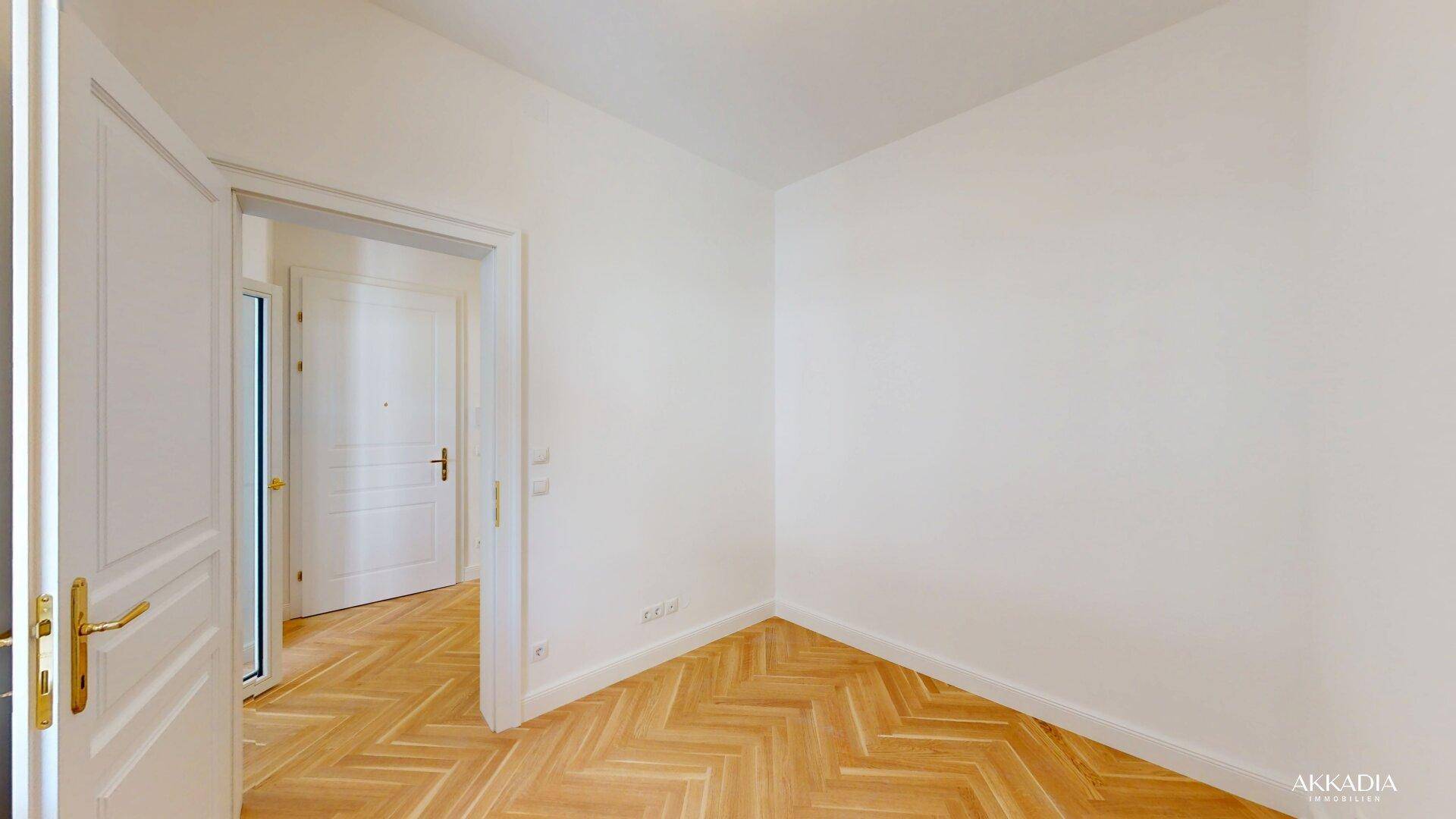 Heller Flur mit Fischgrätparkett und weiß gestrichenen Wänden, der zu weiteren Räumen führt.