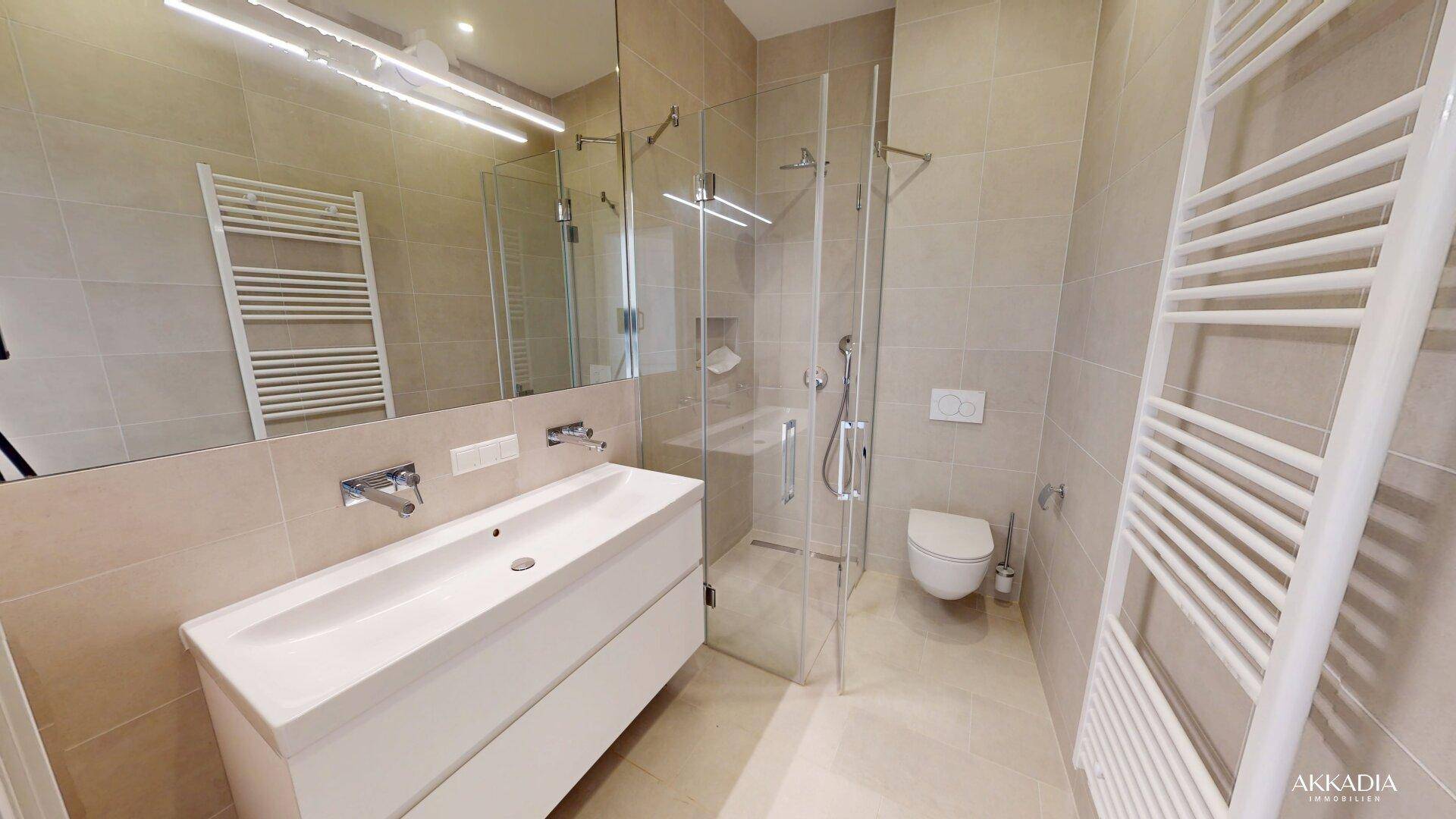 Modernes Badezimmer mit beigefarbenen Fliesen, großem Waschtisch, begehbarer Dusche und Wand-WC.
