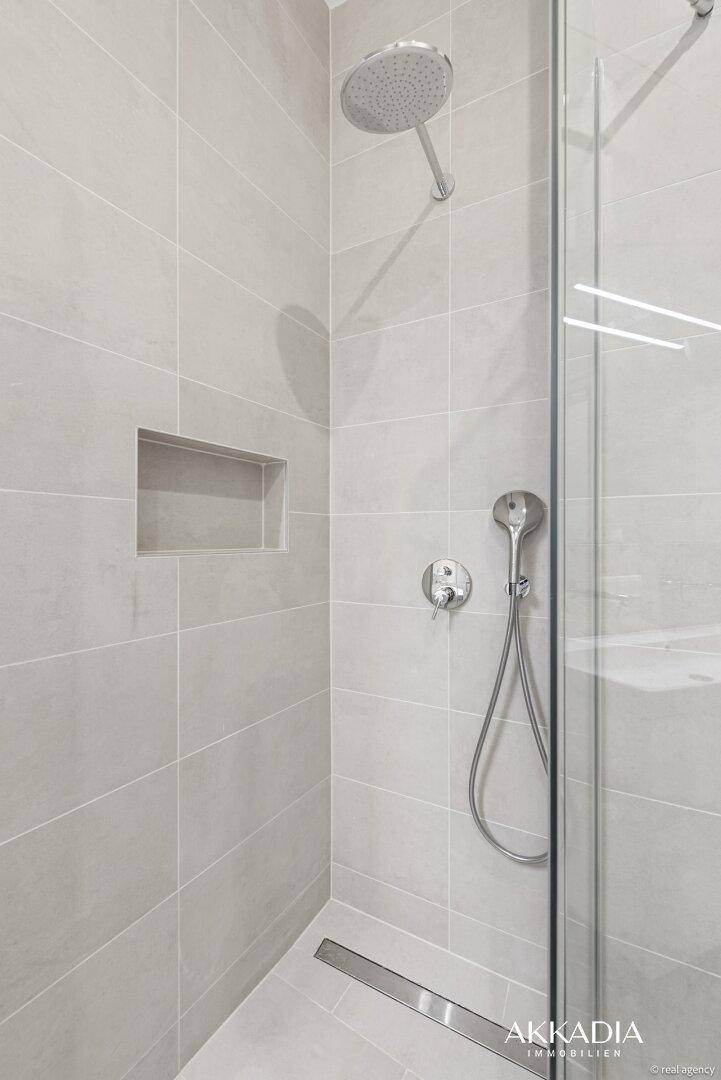 Moderne begehbare Dusche mit Regenduschkopf, hellgrauen Fliesen und praktischer Ablagenische.