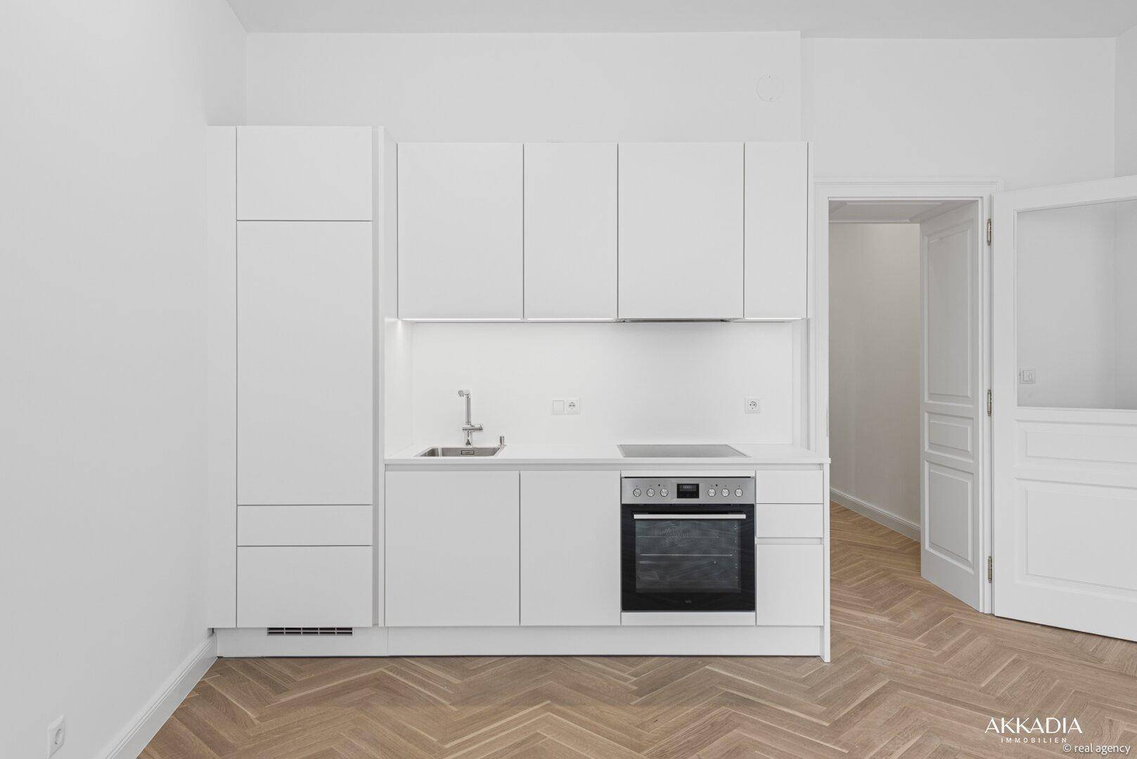 Moderne weiße Einbauküche mit integriertem Backofen, Spüle und Induktionskochfeld auf Fischgrätparkett.