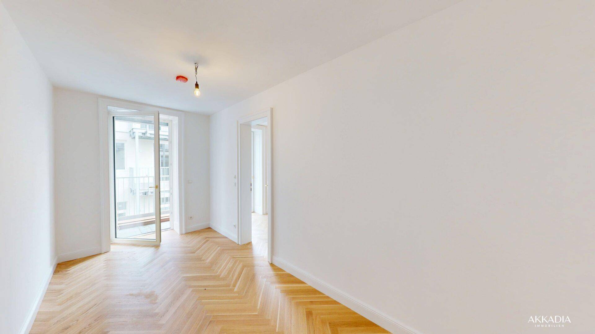 Helles Wohnzimmer mit Fischgrätparkettboden und Zugang zu einem kleinen Balkon.