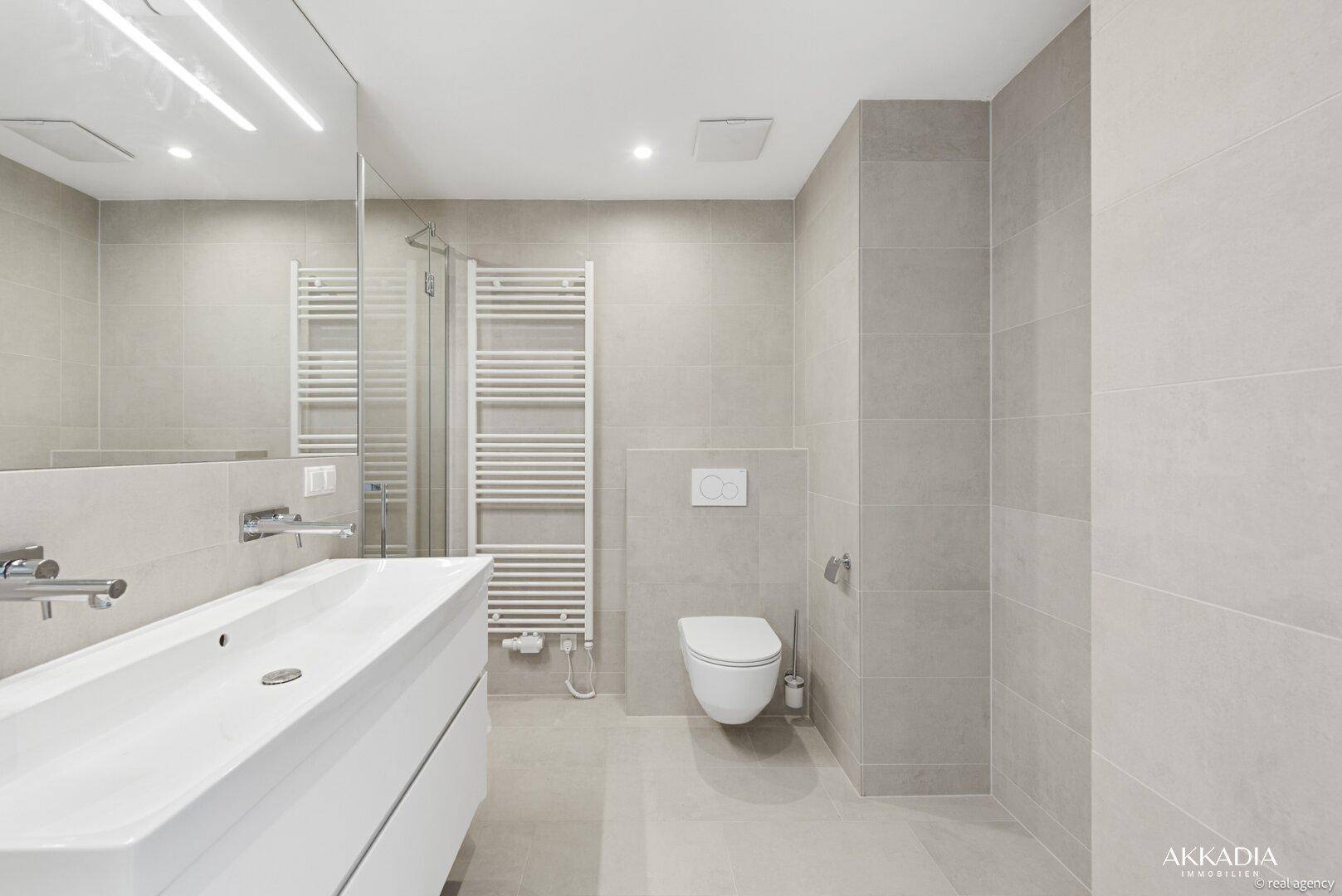 Helles, modernes Badezimmer mit großformatigen Fliesen, Waschtisch und wandhängendem WC.