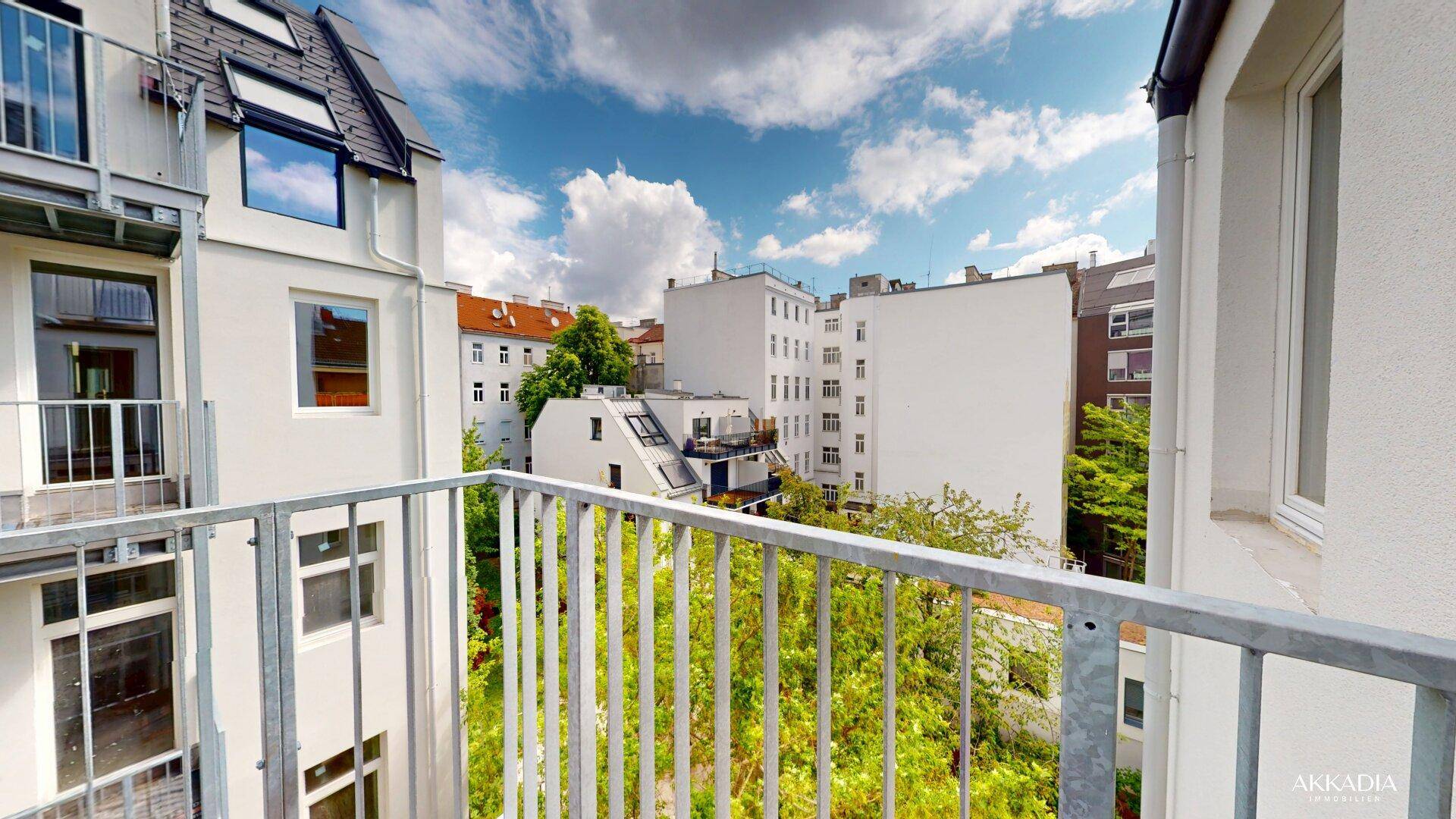 Blick vom Balkon auf den begrünten Innenhof und umliegende Gebäude.