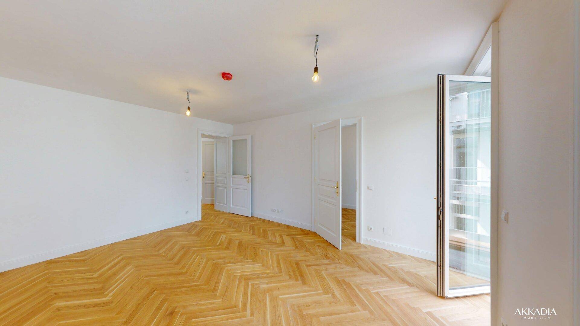 Helles Wohnzimmer mit Fischgrätparkettboden, weißen Türen und Balkonzugang.
