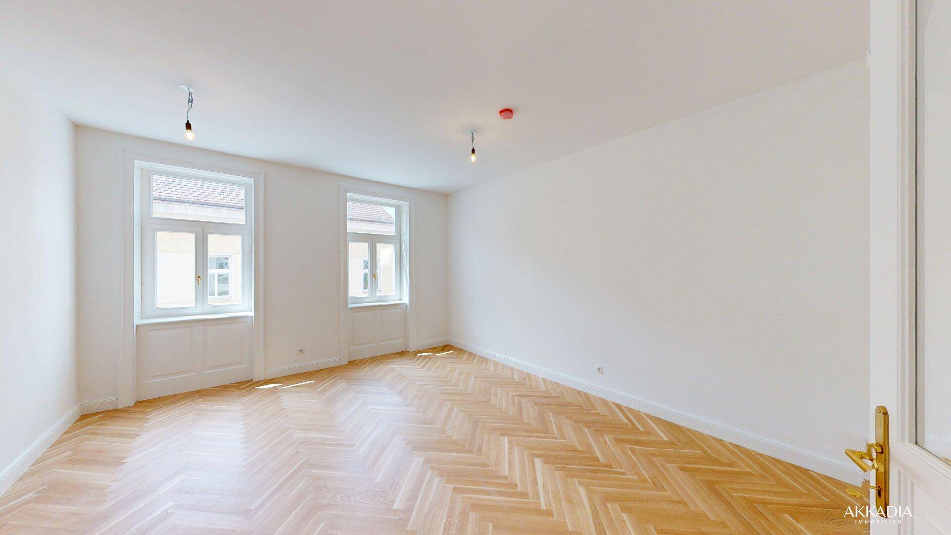 Lichtdurchfluteter Wohnraum mit klassischem Fischgrätparkett und hohen Decken, bereit zur individuellen Gestaltung.