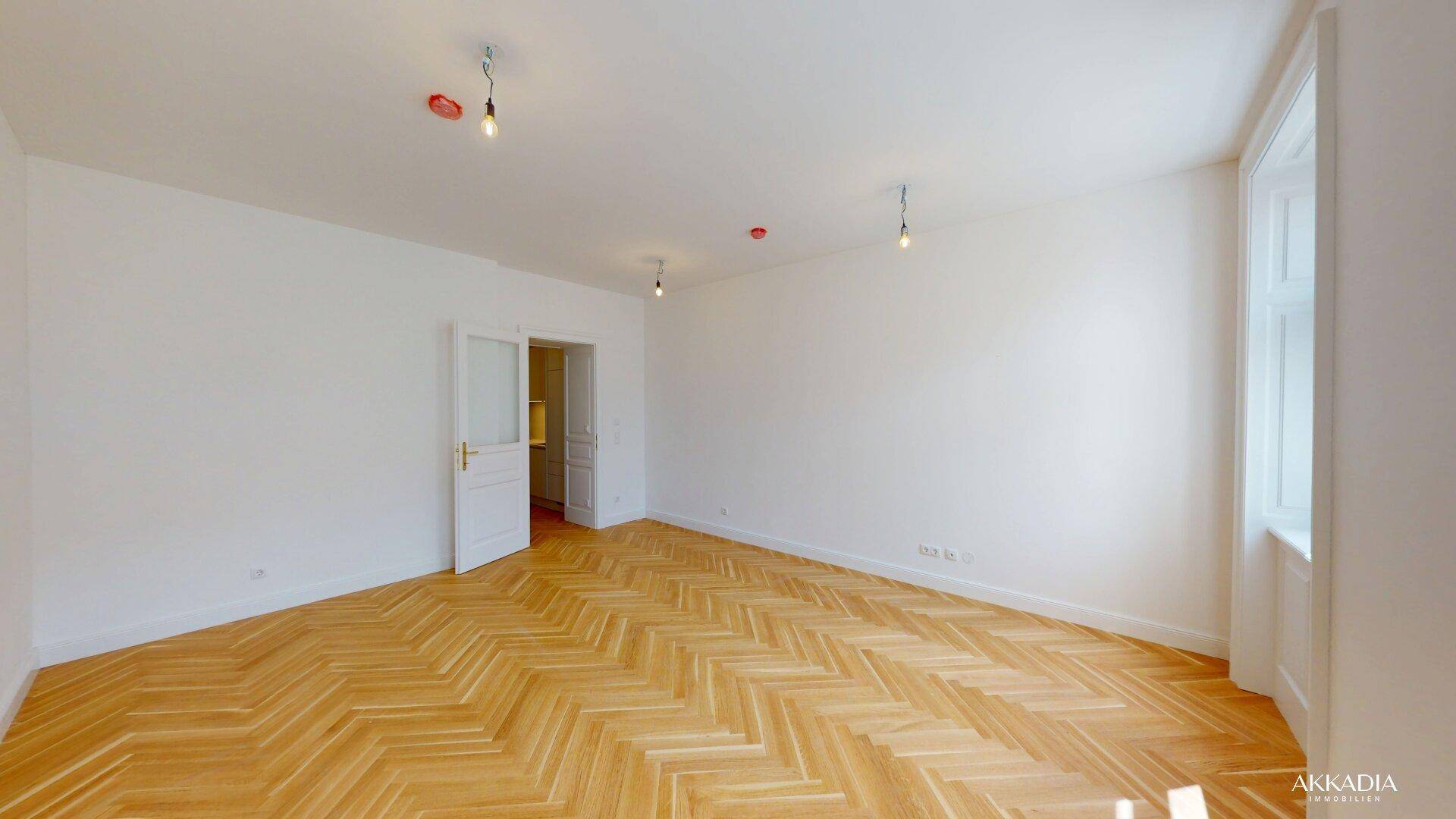 Heller Wohnbereich mit Fischgrätparkett und Zugang zu angrenzenden Räumen, ideal für offenes Wohnen.