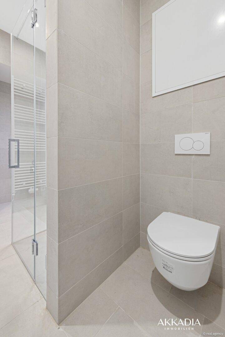 Stilvolles WC im Badezimmer mit wandhängender Toilette und modernen grauen Fliesen.