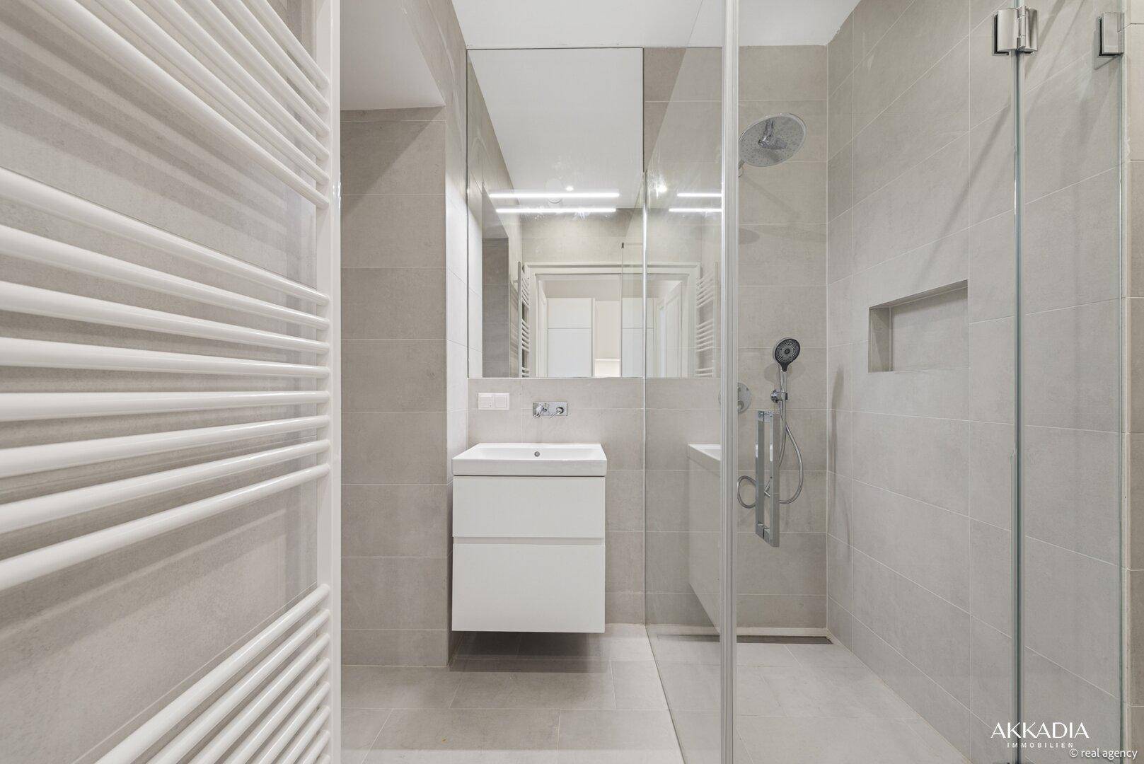 Modernes Badezimmer mit begehbarer Dusche, eleganten grauen Fliesen und beheiztem Handtuchhalter.