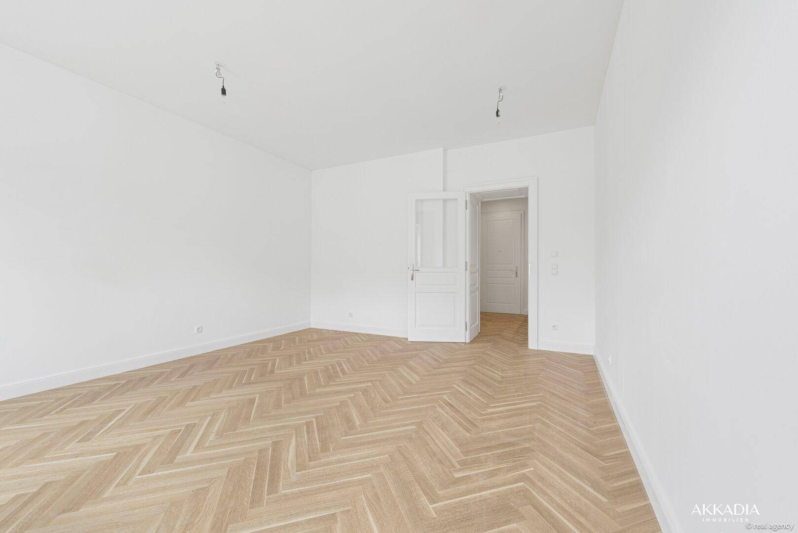 Geräumiger Wohnraum mit hellem Fischgrätparkett und Zugang zu weiteren Zimmern, ideal für flexibles Wohnen.