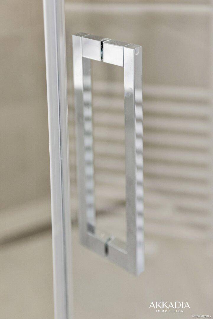 Detailaufnahme eines modernen, glänzenden Griffs an einer Duschkabinentür.